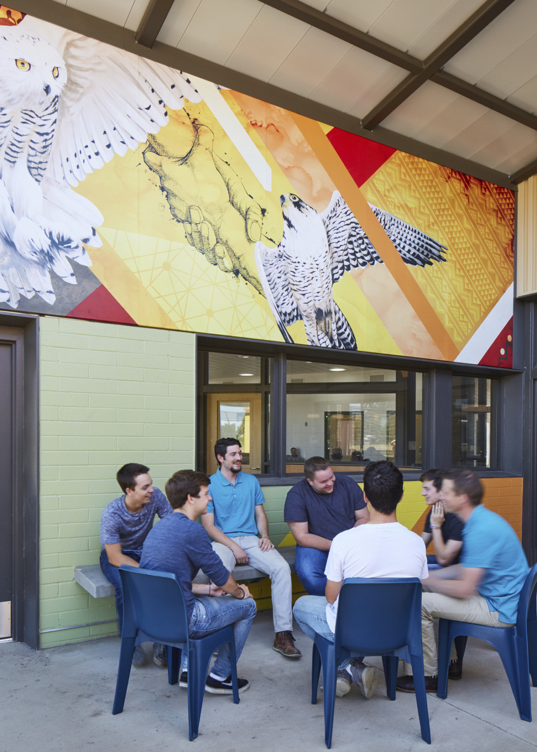 Seating against green, yellow, and orange colorblock wall with interior window. Above, a mural of owls, interlocking hands