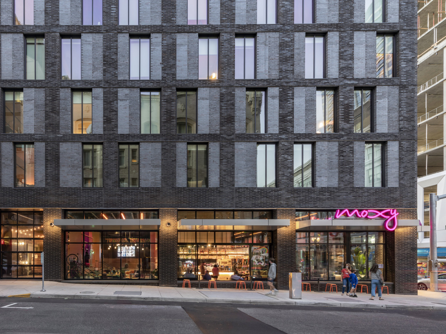 Closeup view of lobby and 1st 5 stories. Lobby has floor to ceiling windows with grey flat awnings separated by brick columns