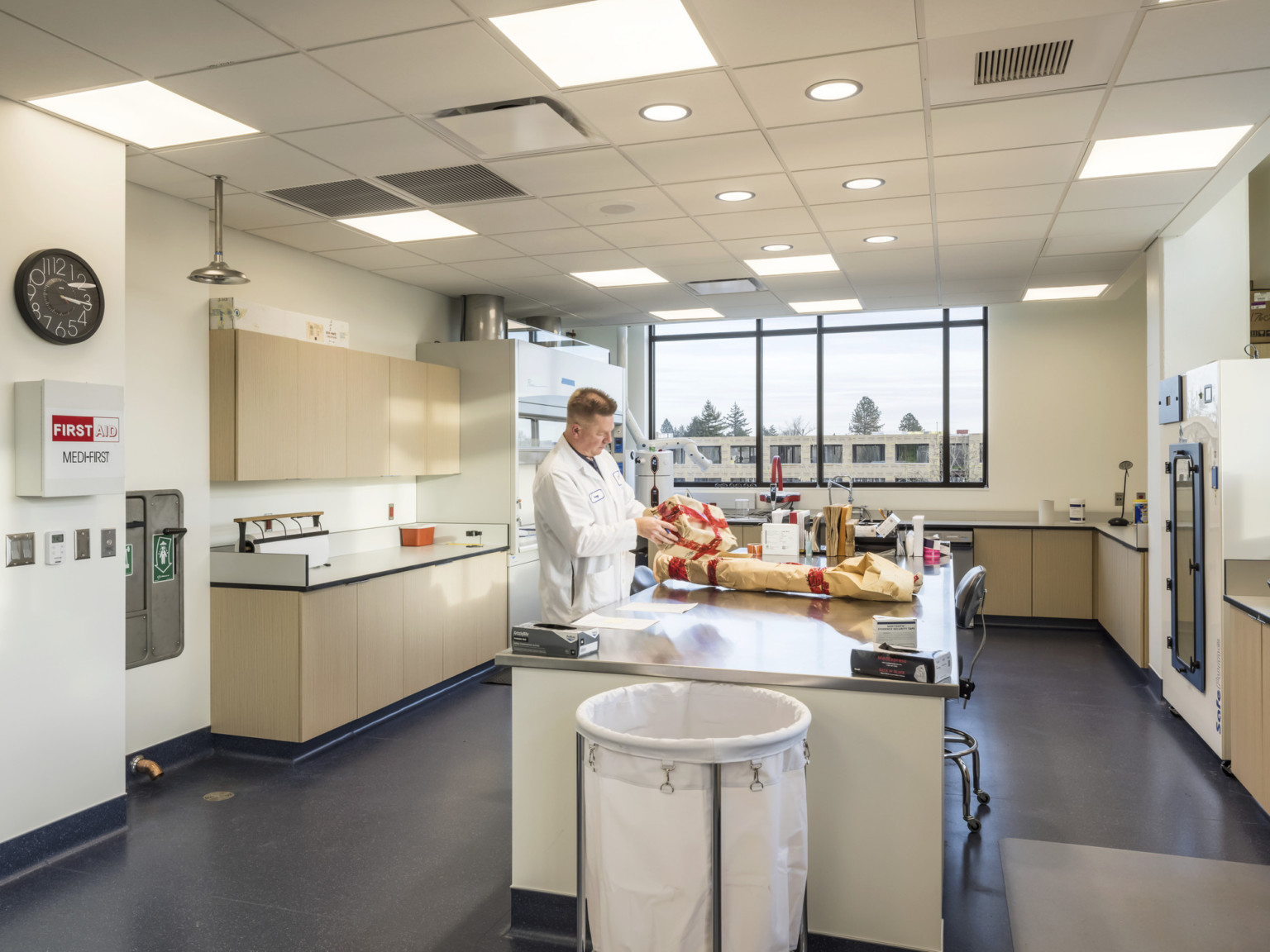 Police lab with large central island. Counter space lines the room around lab equipment. A man in a lab coat stands by island