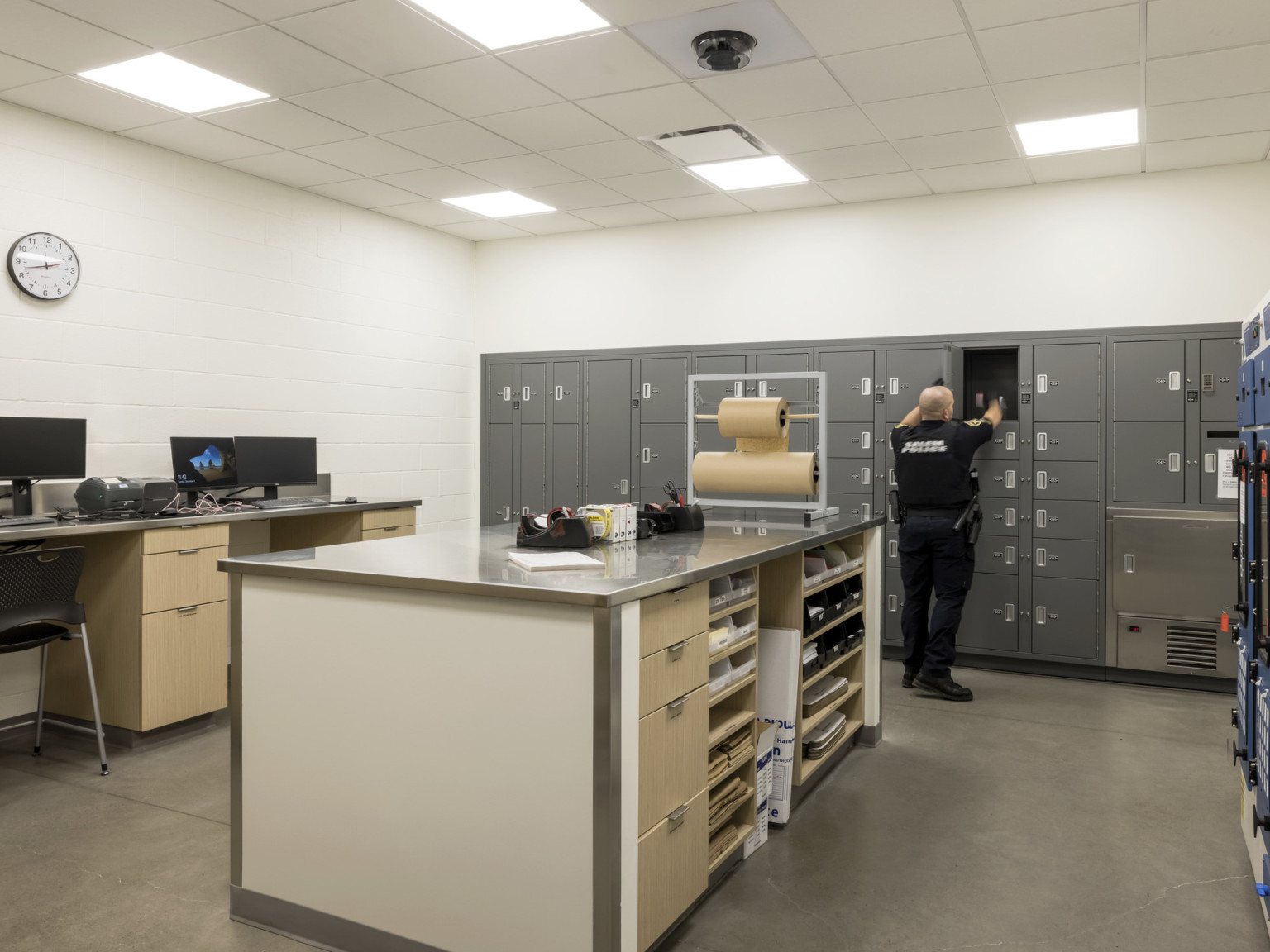 Storage lockers along wall with island counter for work space with tape and paper supplies. Computer and printer sit on desk