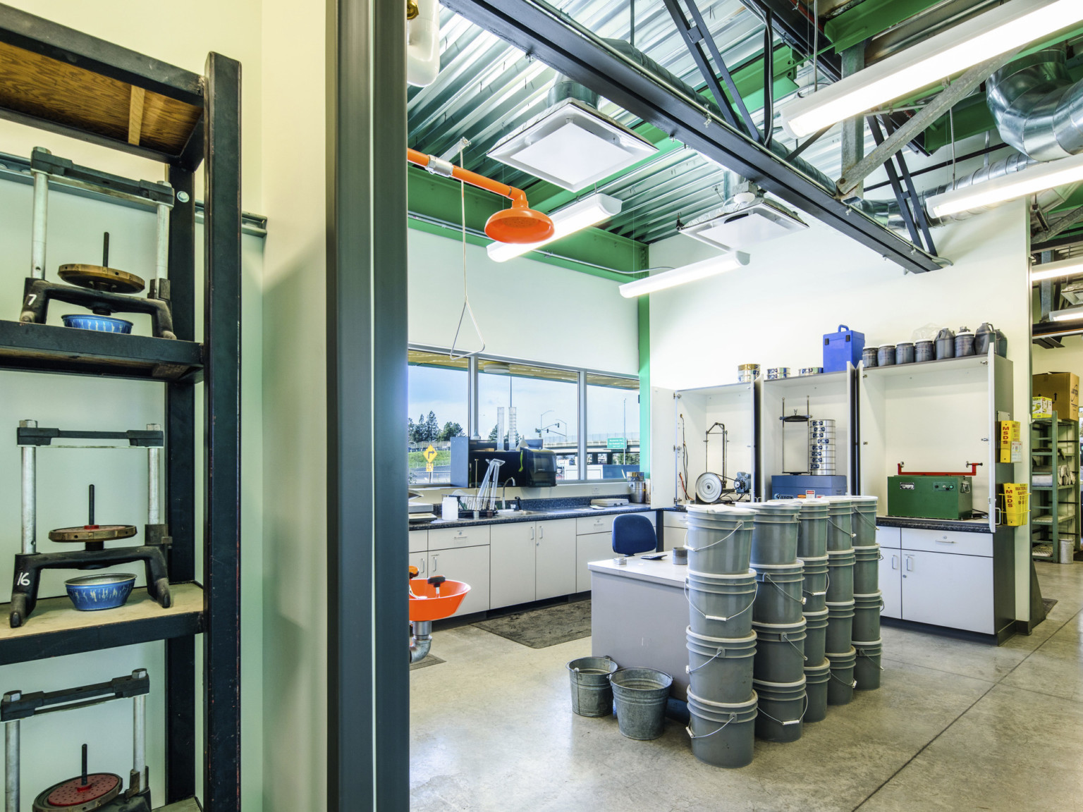 White room with green ceiling. Equipment on shelves, and a desk, center, partially obscured by stack of grey buckets