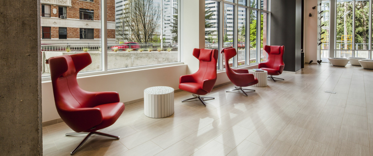 Red chairs with round side tables in a white room with black accent column and large window looking out to street level