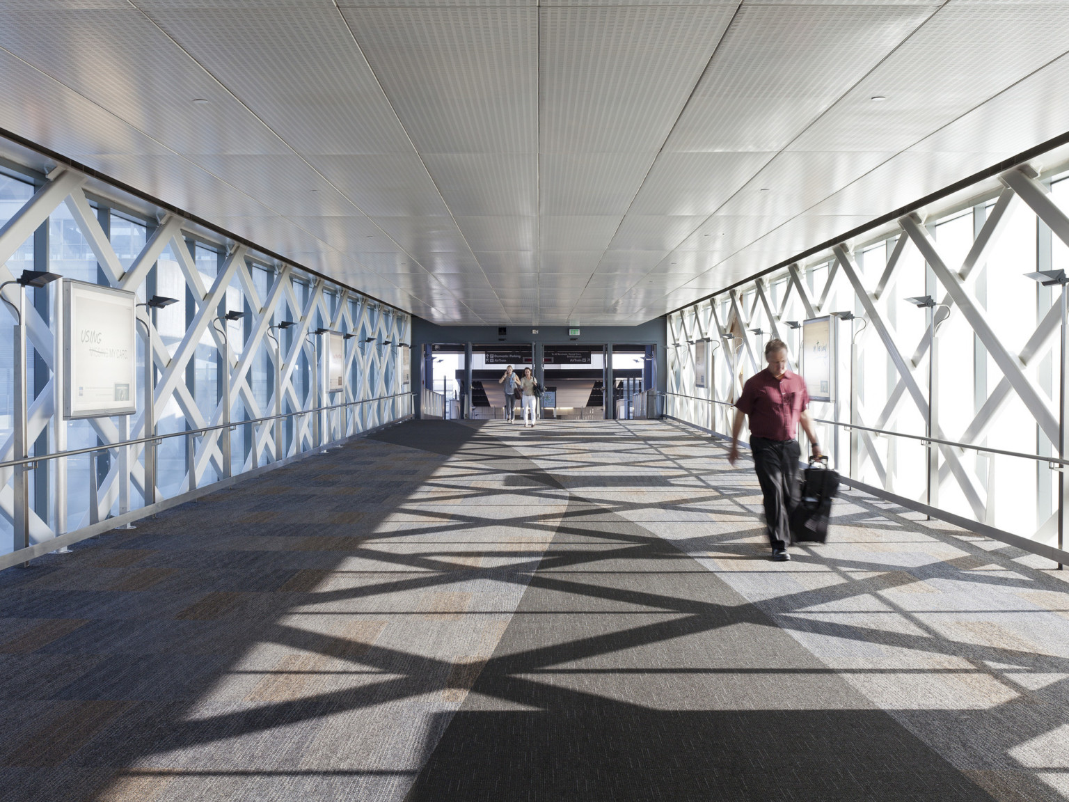 Glass walled skywalk with large scale lattice details. White panel ceiling and carpeted floor