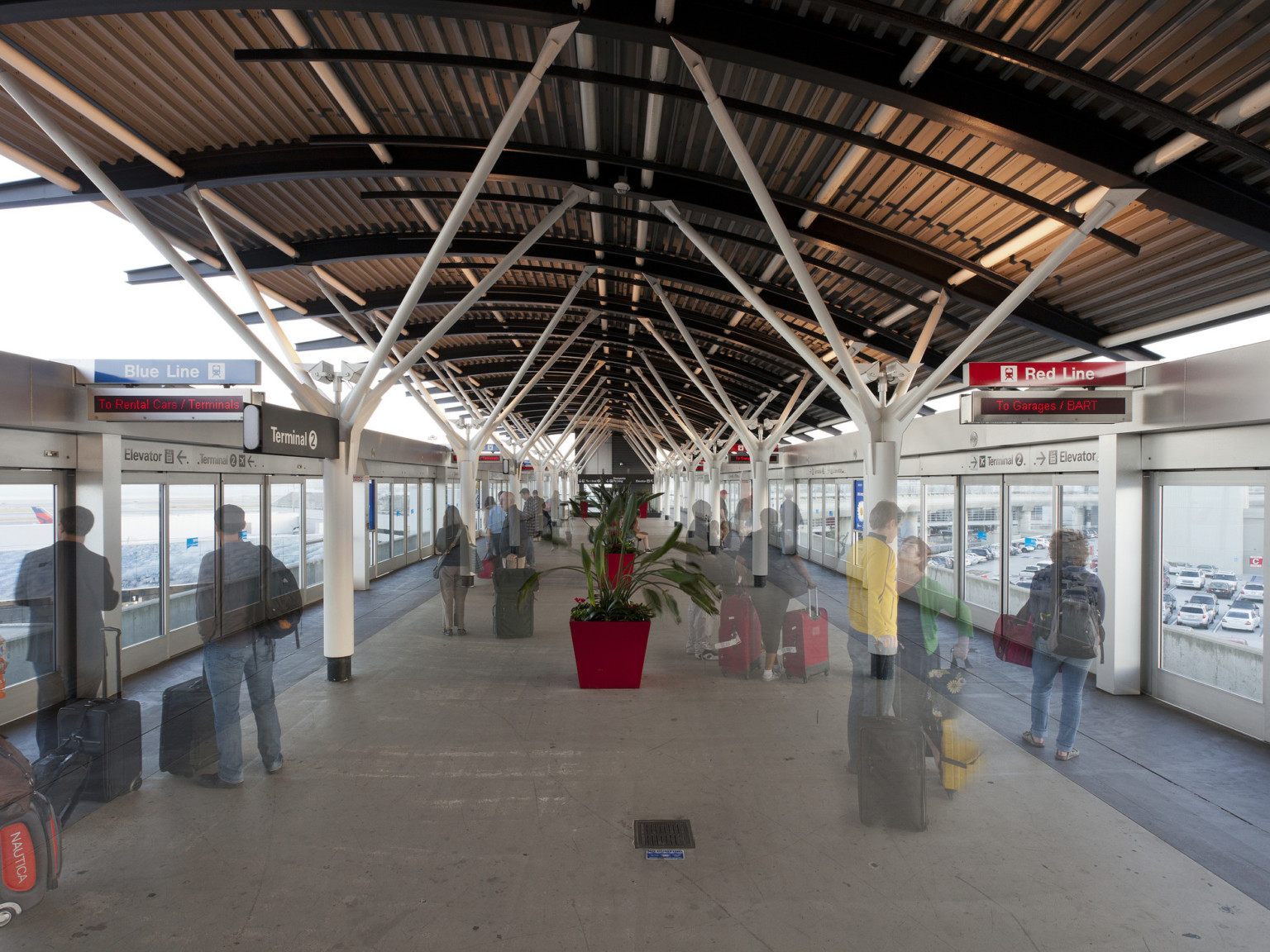 Glass walls with sliding doors and signs on either side of AirTrain station. Black canopy above with columns, exposed beams