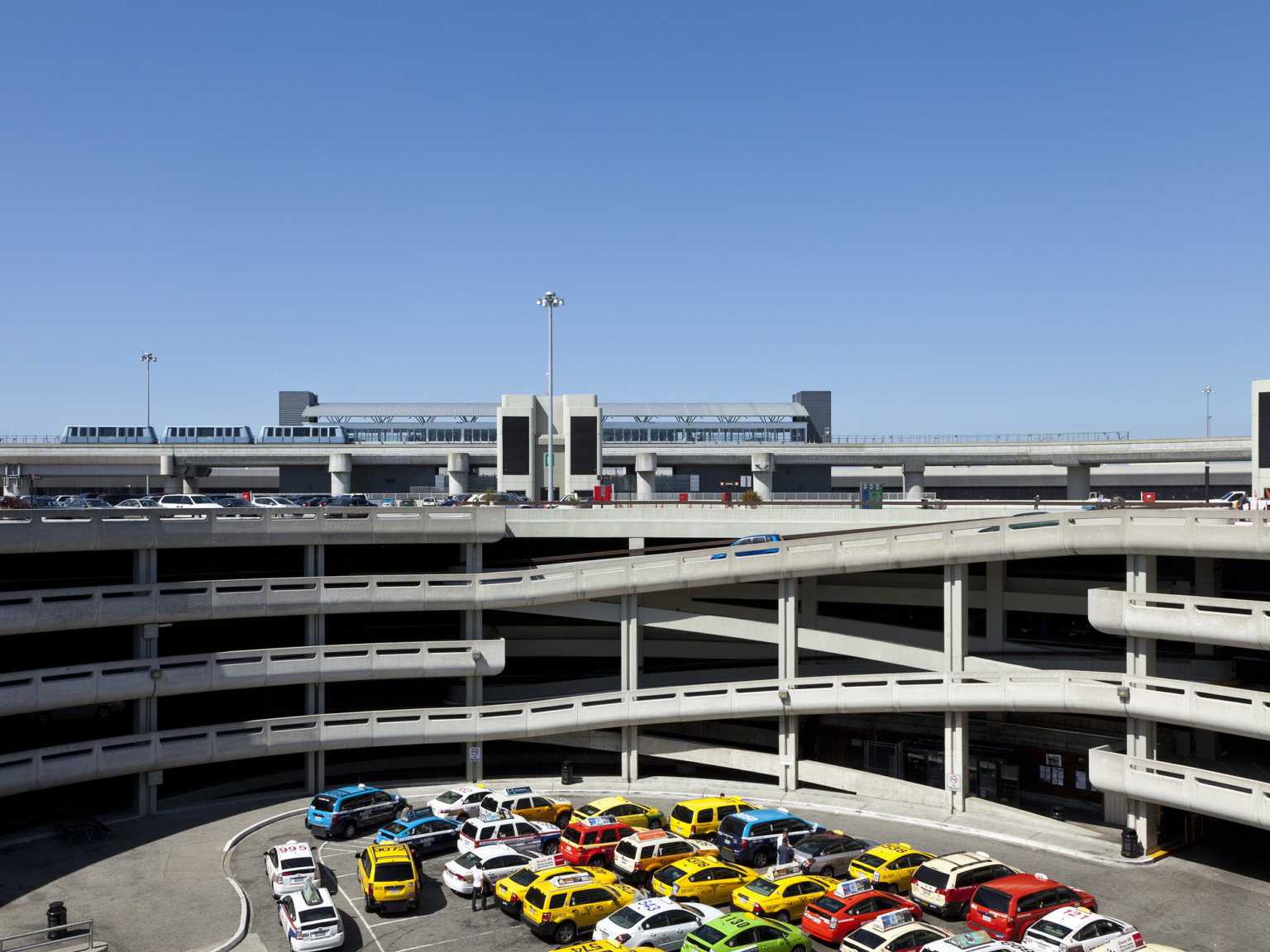 Taxi zone in open space in the middle of the ground level of parking garage with airtrain station on roof