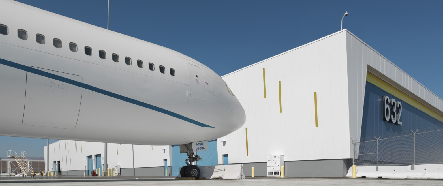 Corner view of blue and yellow building with white wrapped facade with yellow accents on side facing plane with loading doors