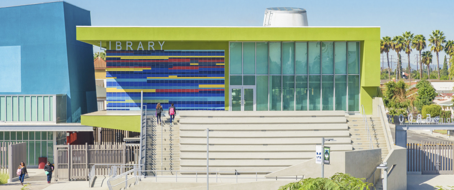 Closeup of lime green building labeled Library. Stairs on sides of step benches. Multicolor tile by recessed glass entrance