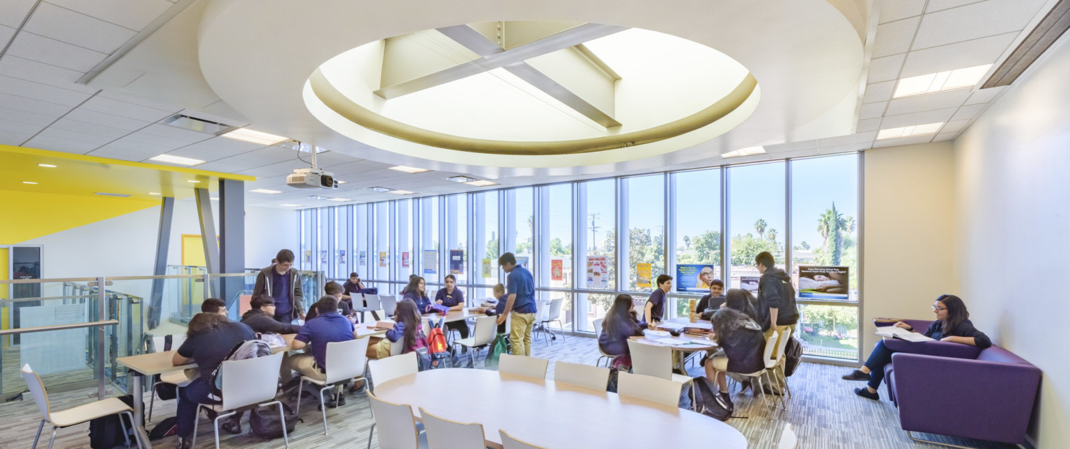 Floor to ceiling windows in white room with tables and chairs. Round recessed ceiling detail with exposed beams and lighting