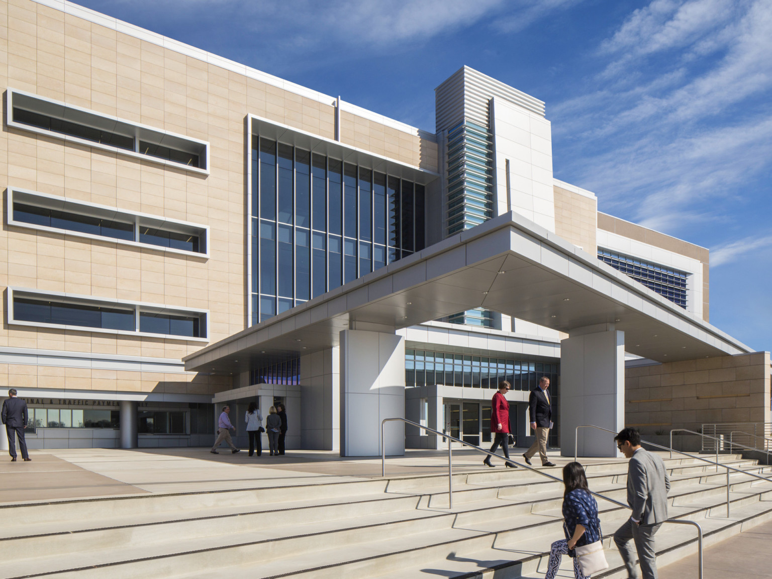 Exterior view of entry. Stairs lead up to plaza, partially covered by angled grey structure. Large windows at building center