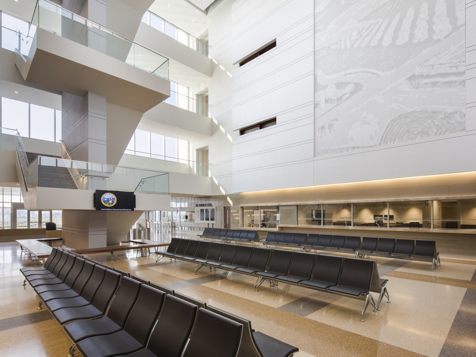 Large seating area below stairs in atrium. Entry doors to the back right. White wall with carved mural above interior window