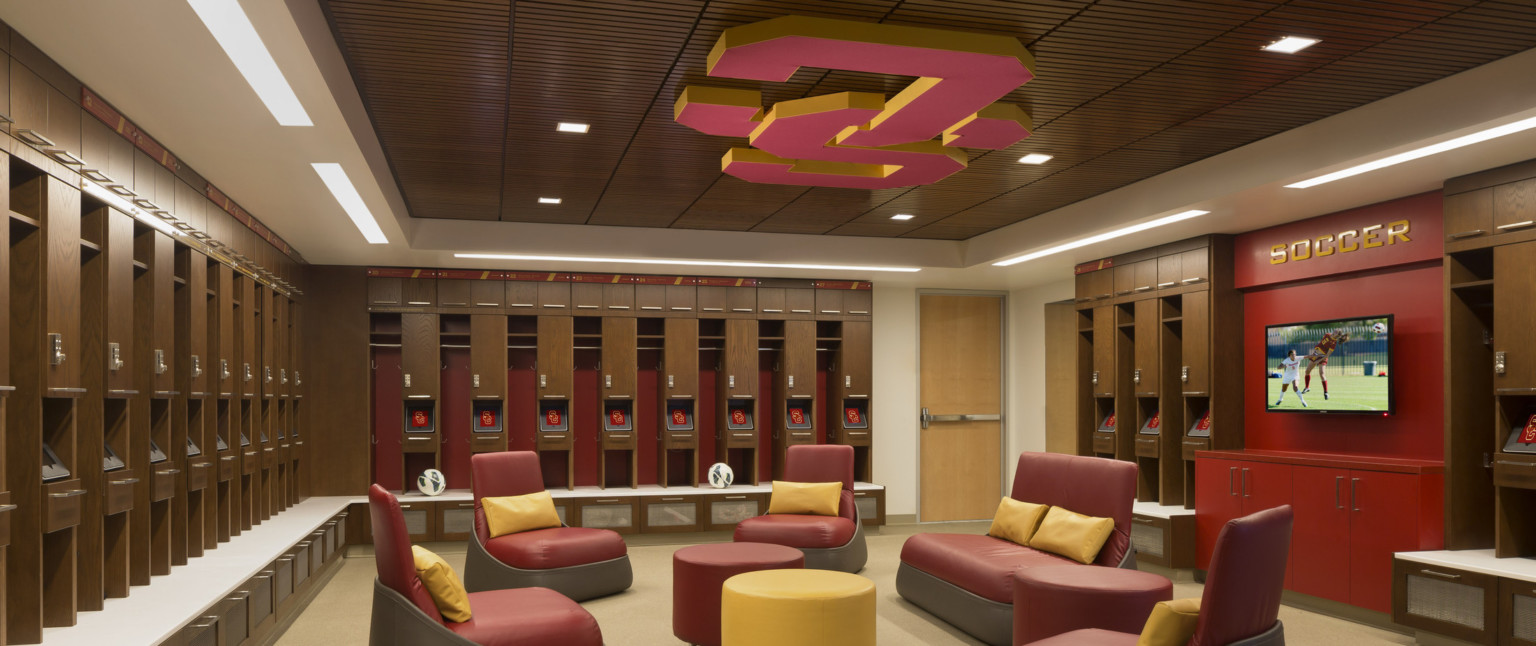 Wood lockers with seating bench line room with recessed wood panel ceiling and red SC logo. Seating area by red accent wall