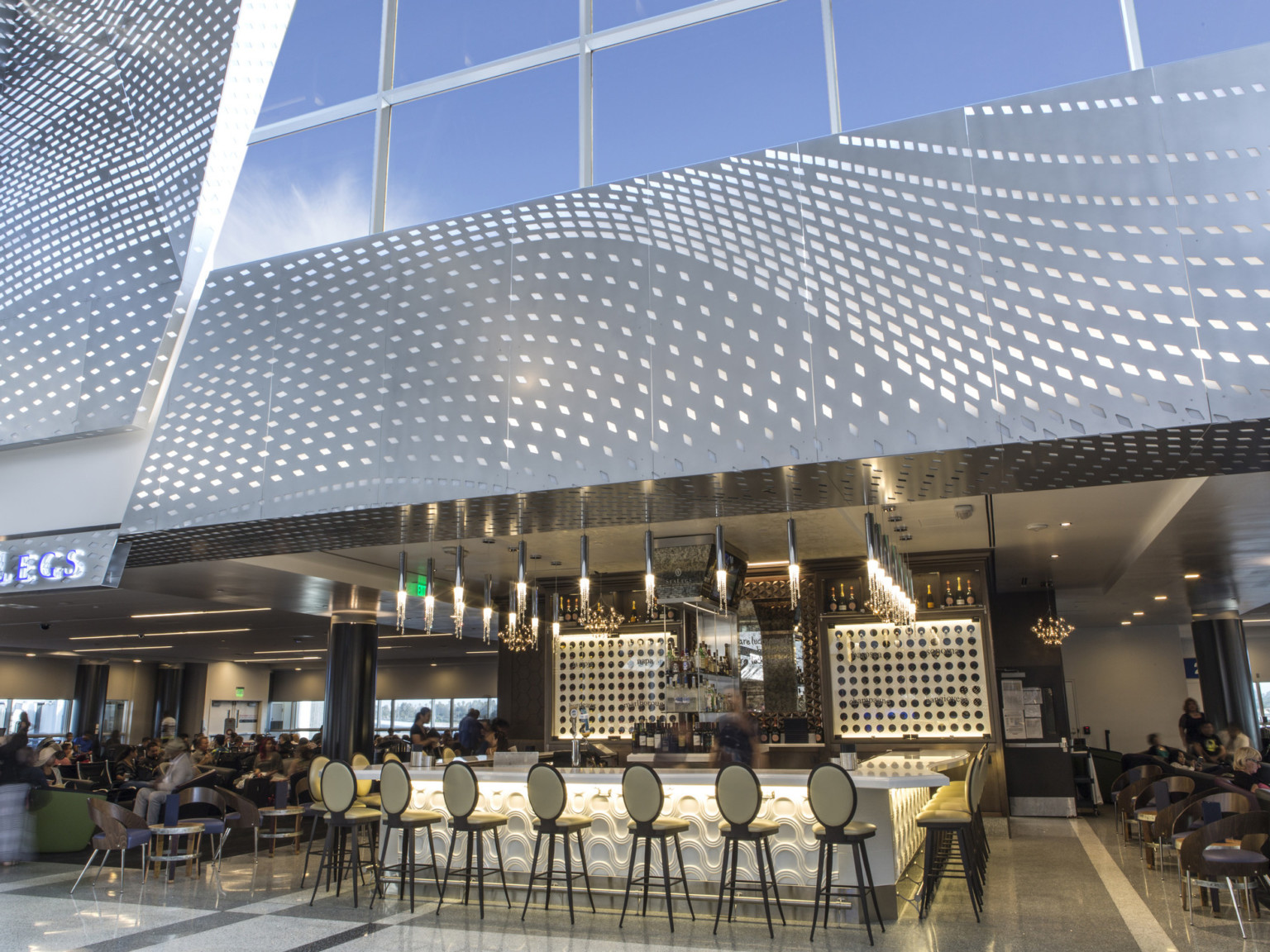 Recessed dining space in double height room with illuminated bar, center, under silver perforated wall accent and windows