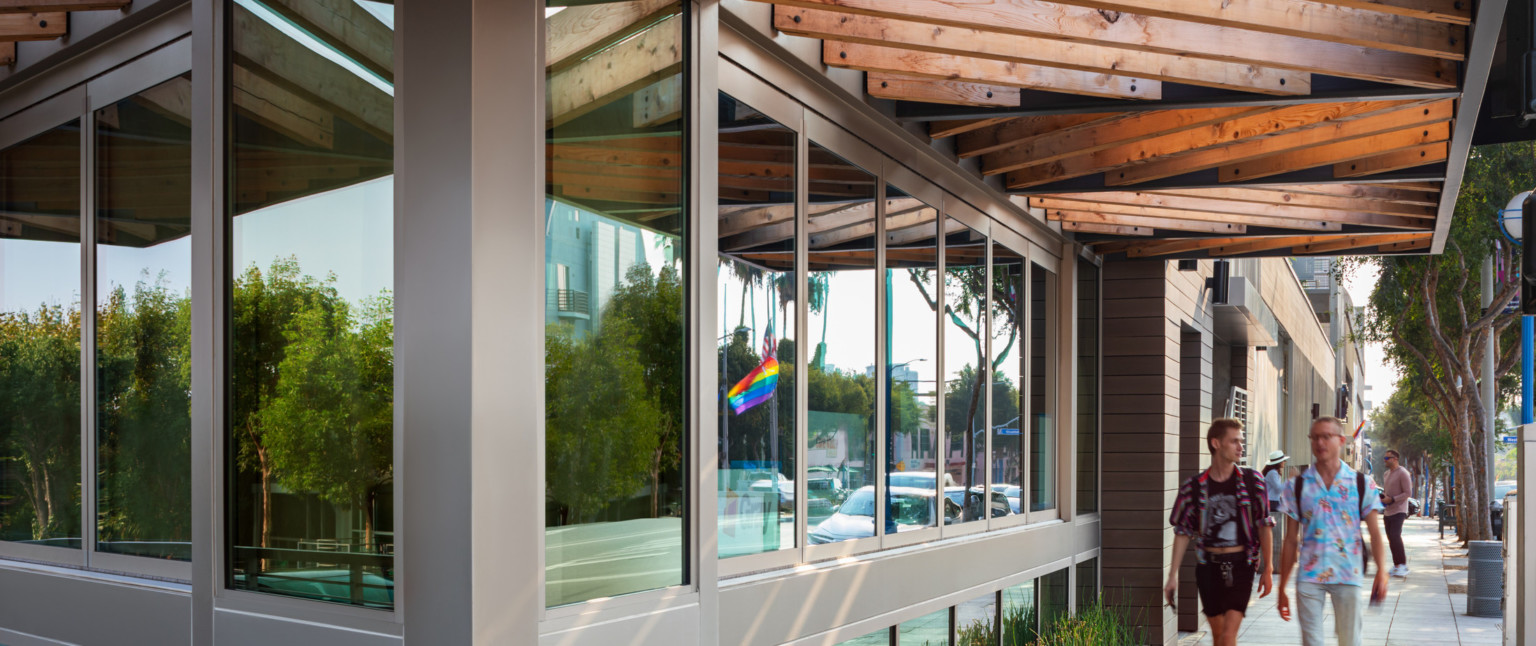 Corner of building with window walls on each side with silver seams under an awning with exposed wood beams