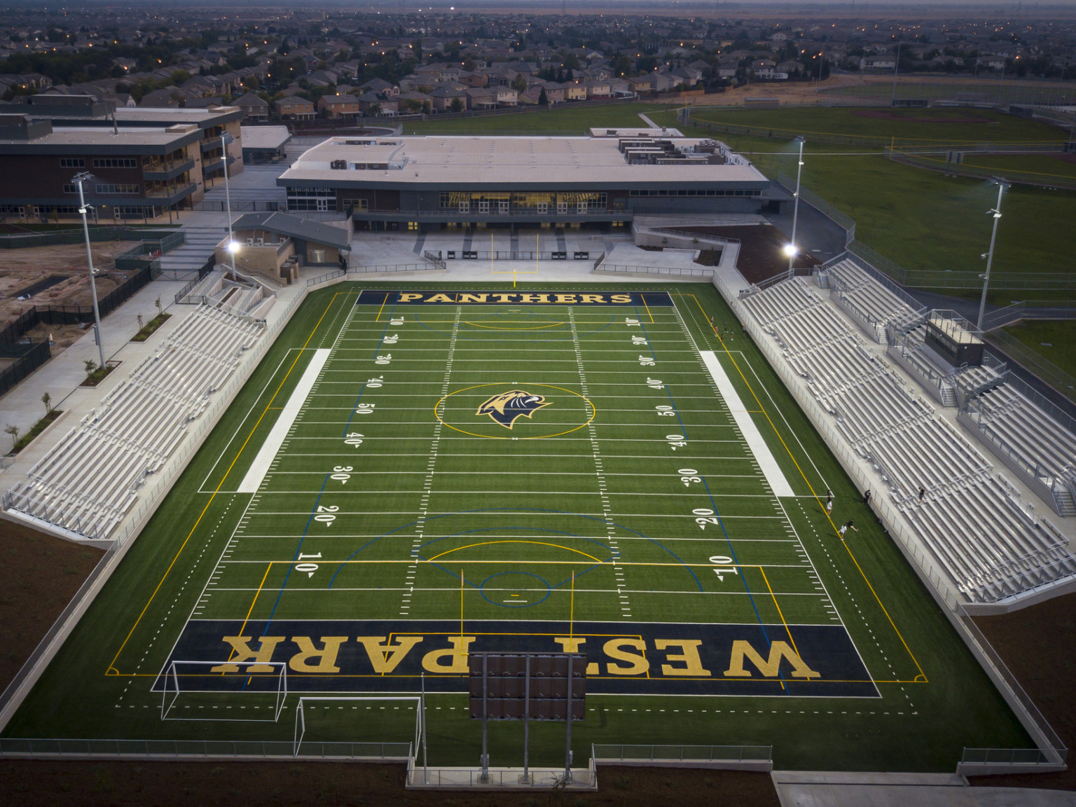 Aerial view of football stadium with West Park Panthers written across blue end zones. Sideline seating with building across