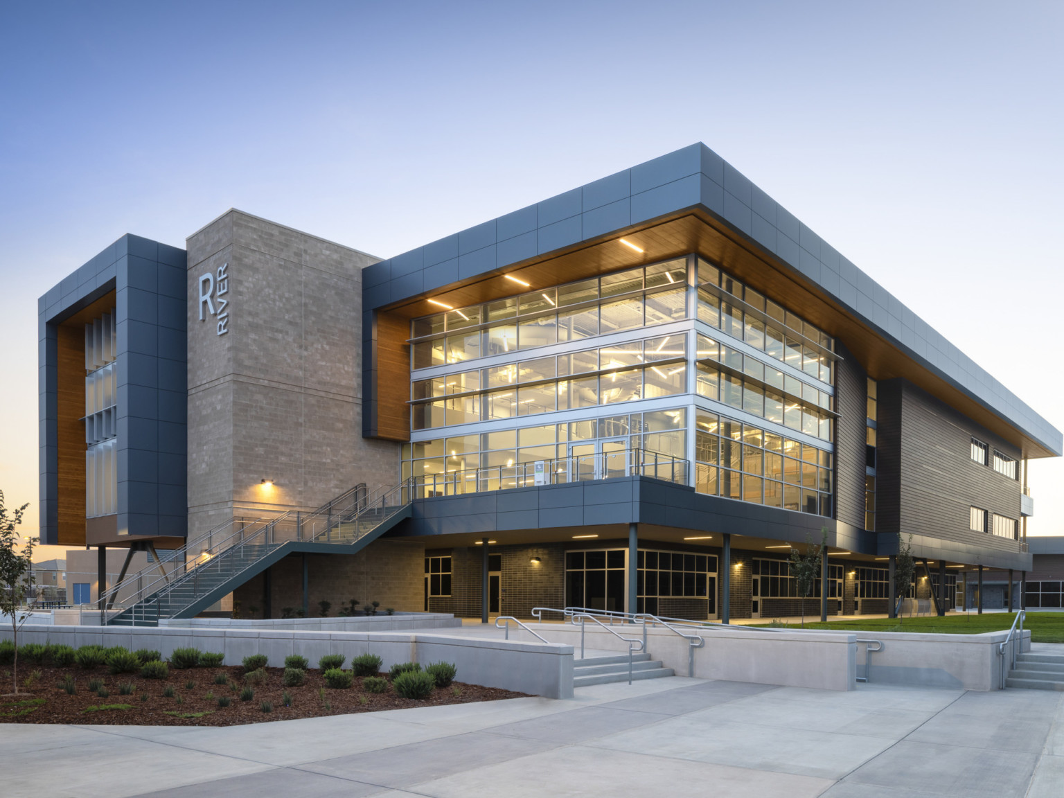 Corner view of River building with double height windows wrapping around side. Canopy wraps around windows with wood accent