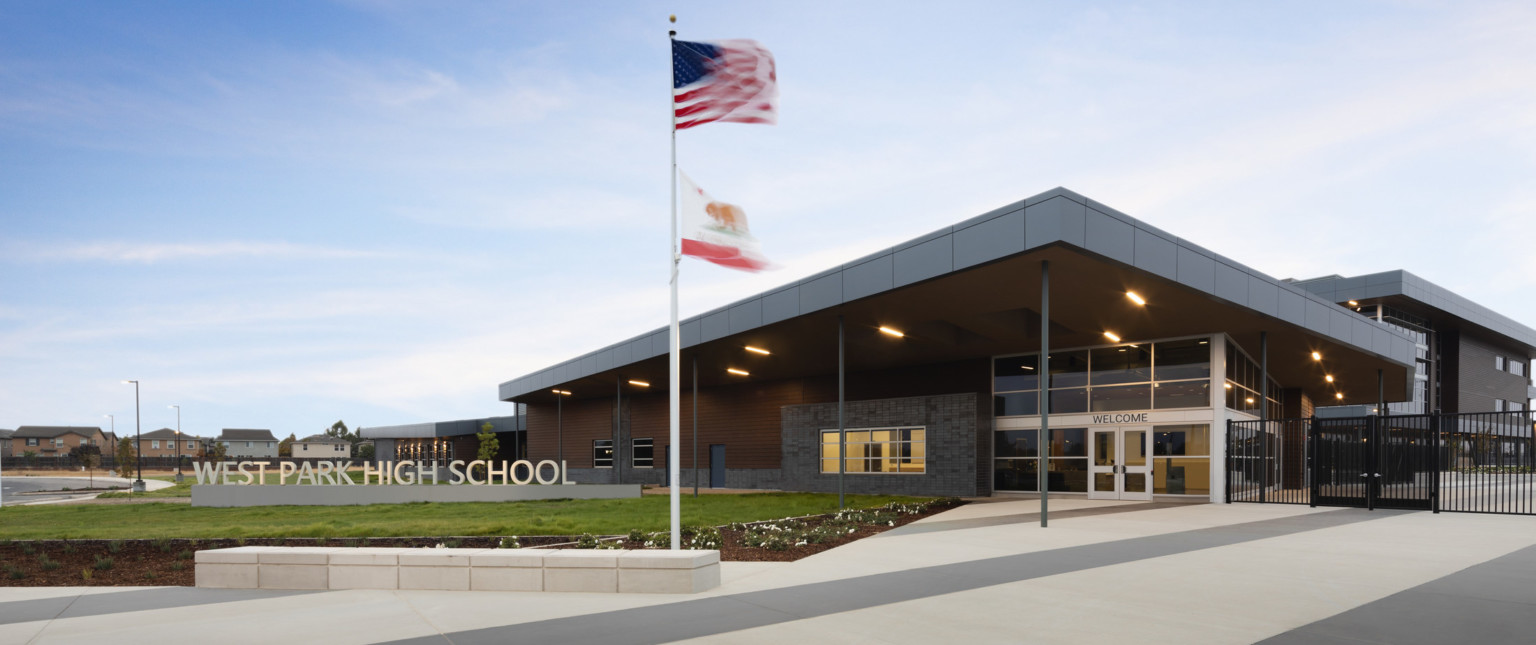 West Park High School sign in front of single story building with large angled canopy extending towards flags in plaza