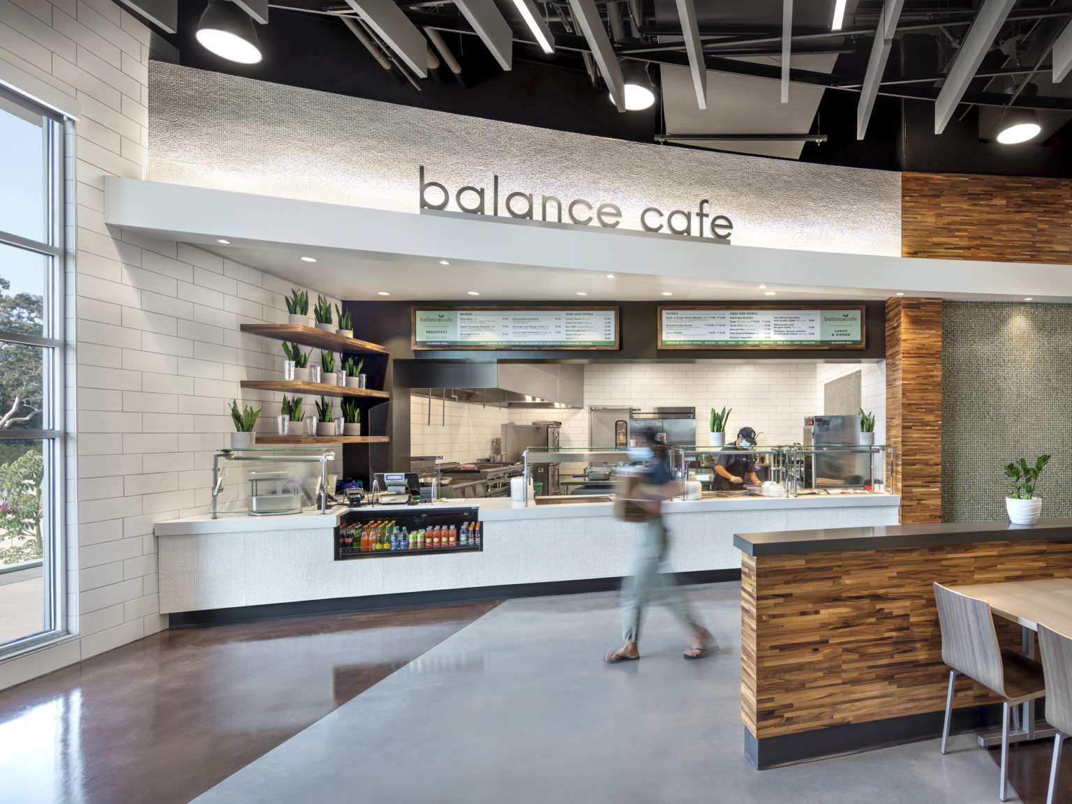 Wood counter separating dinging area from white tiled Balance Cafe food station next to wood food station