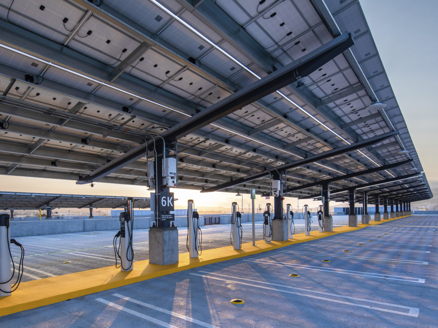 Electric vehicle charging stations under solar canopy supported by black beams on roof of garage