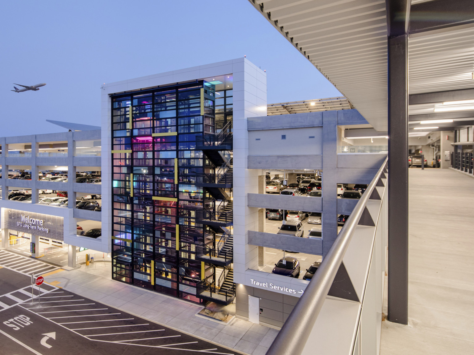 View from skywalk over road connecting to garage at 5th floor. Entrance to left, past glass tower. Plane flying above