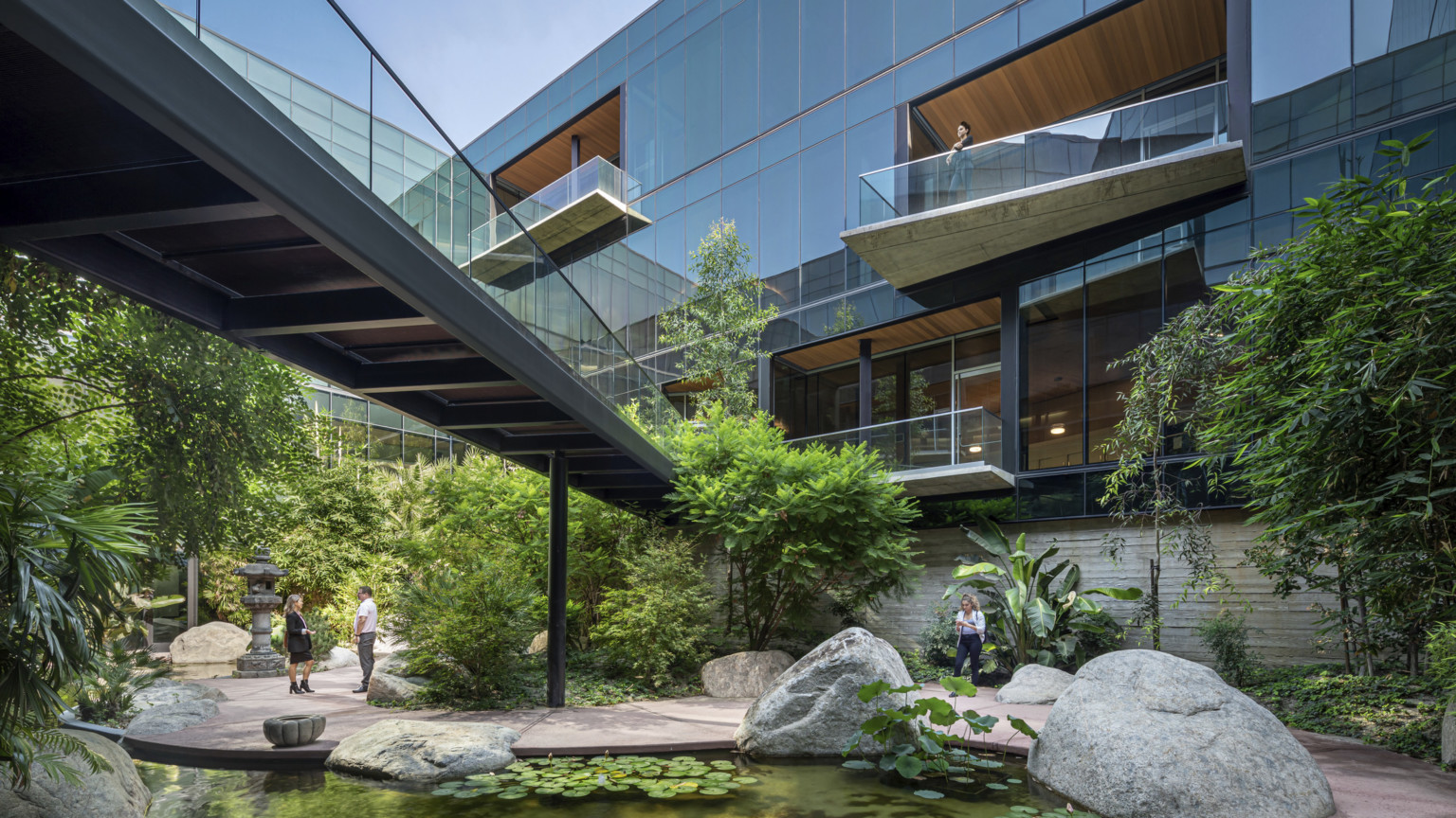 ESRI Campus front courtyard expansion. Angled overhanging balconies on a glass building with bridge over courtyard garden