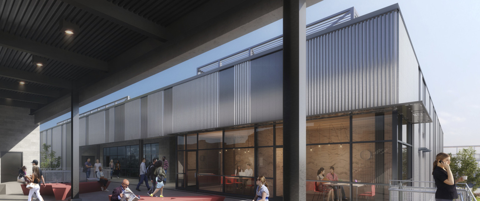 Exterior path with views into glass walled learning spaces with tables and chairs. Grey siding above with flat awning between