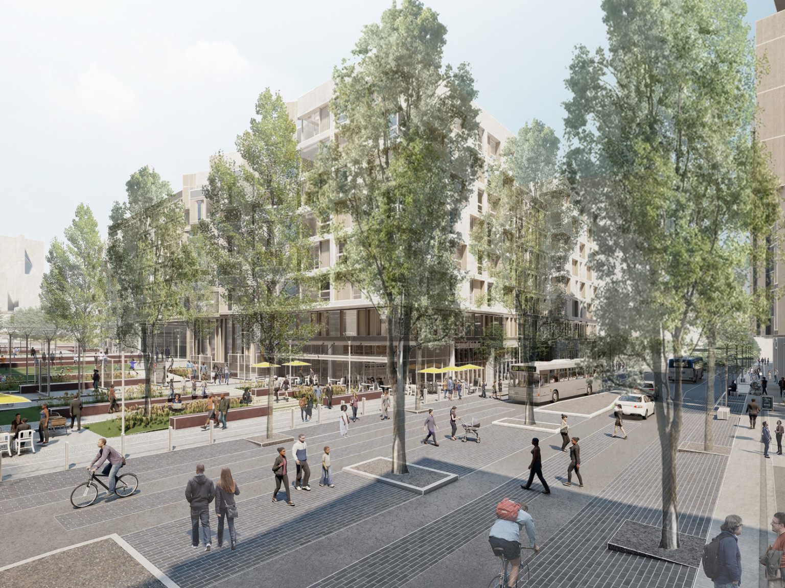 Corner view from across a pedestrian friendly street. Trees along sides of street and median. Outdoor seating and green space