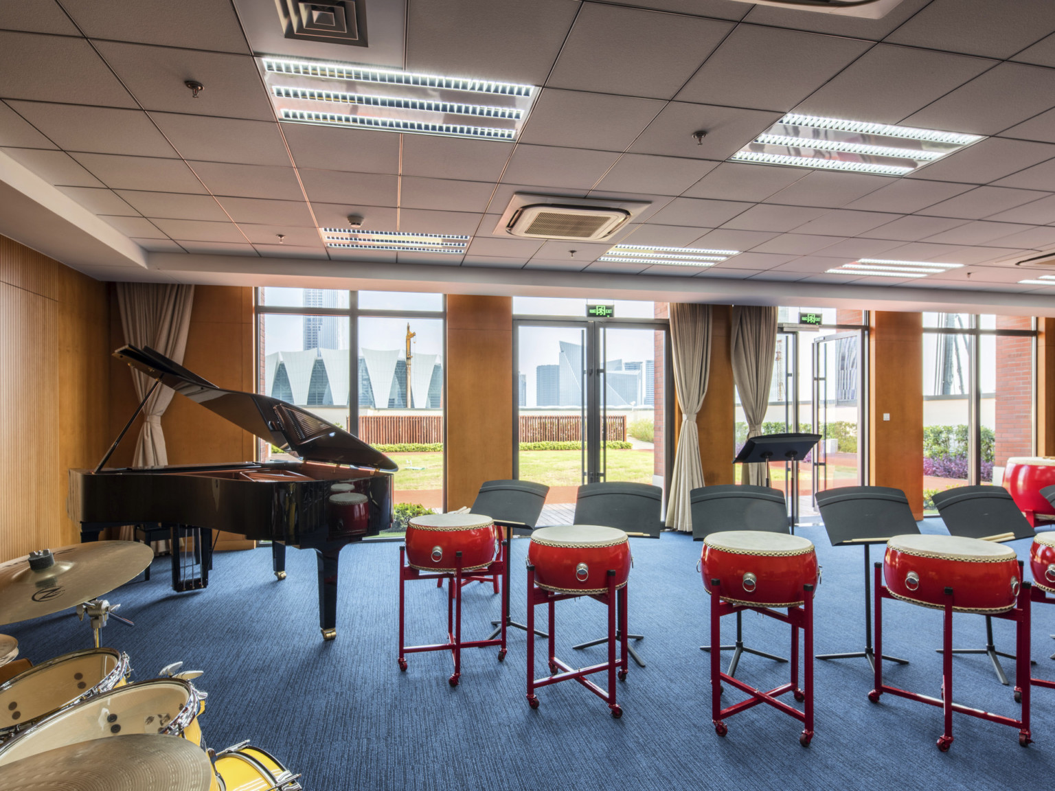 A music room with wood walls, floor to ceiling window panels, and glass double doors opening out to the lawn with a city view