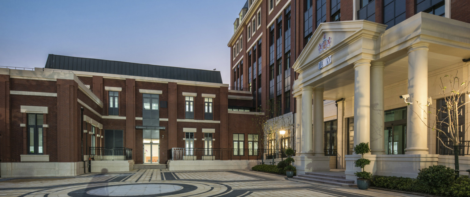 Courtyard view of white stone front entry with framed with columns around glass doors. 2 story brick building connects left