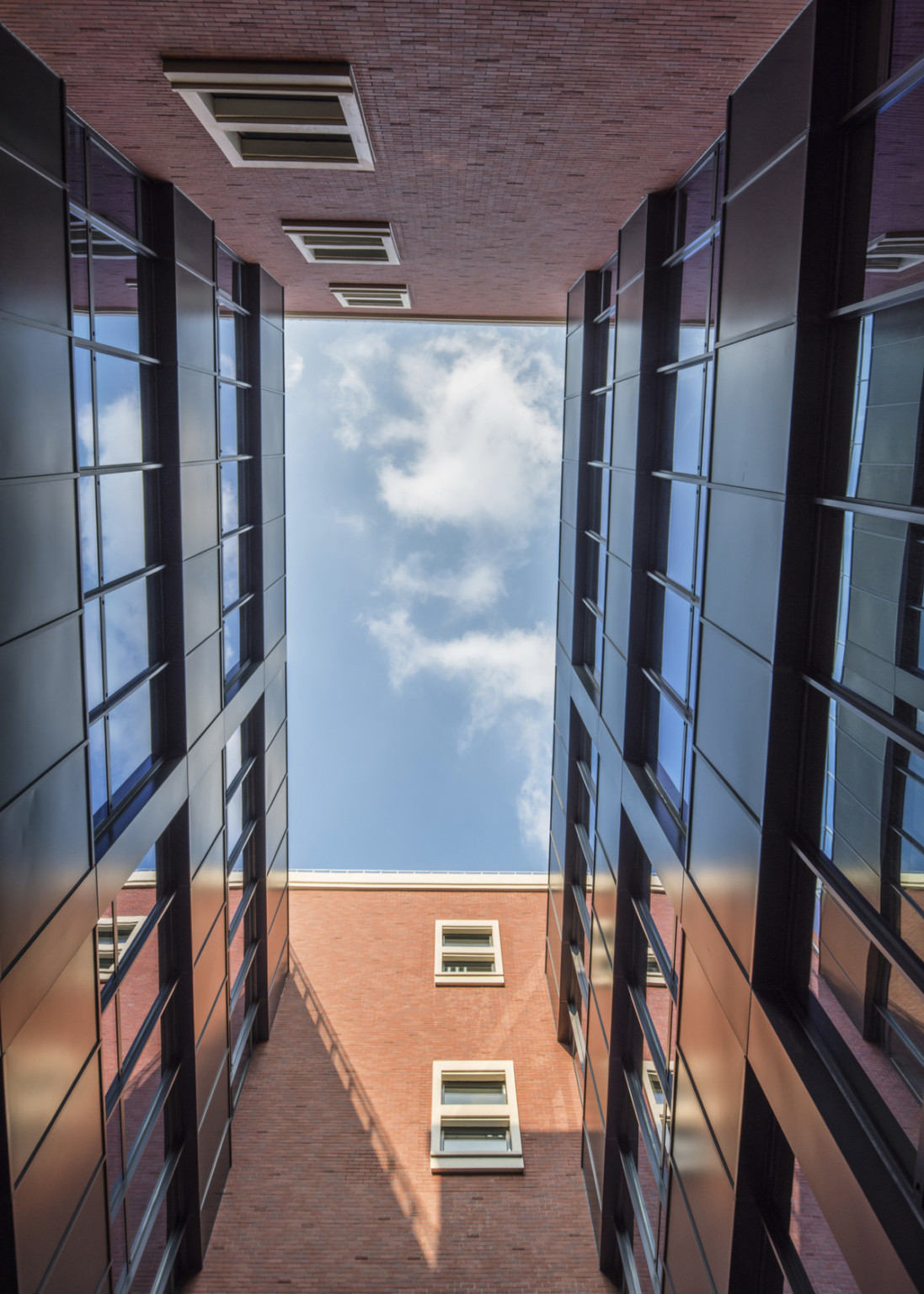 View between buildings looking upward. Brick walls with white windows, front and back. Black walls with windows, either side