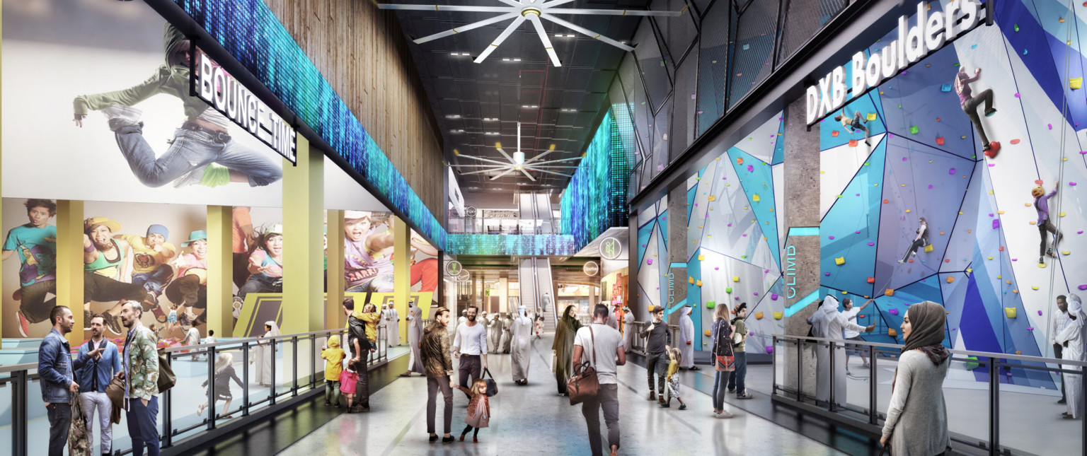 Double height hallway leading to escalators. Rock climbing wall, right. Strip of LED lights run along left wall and 2nd floor