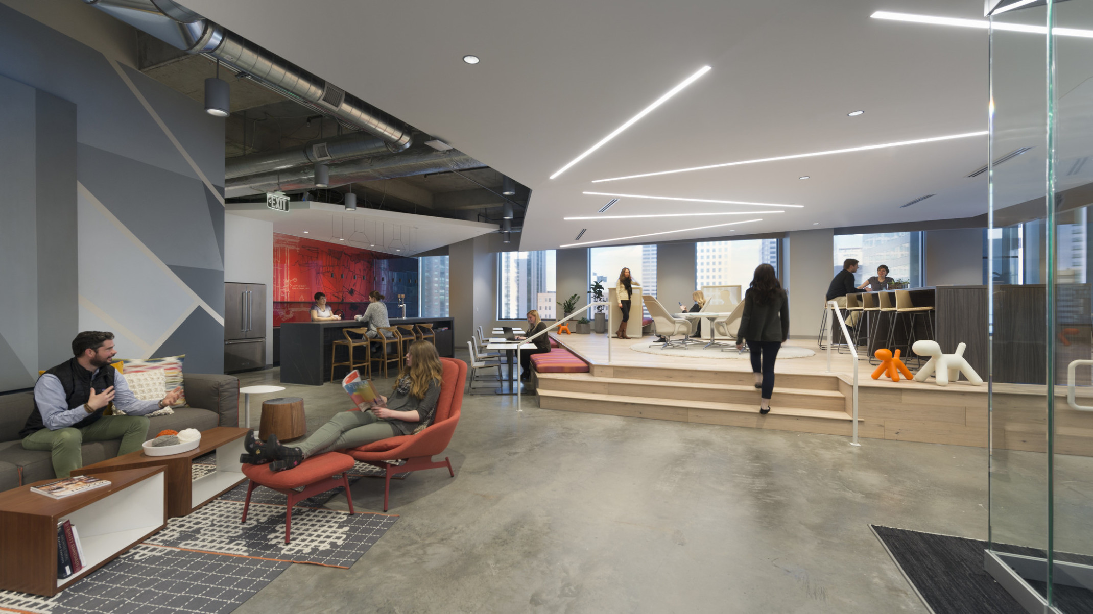 people conversing in clusters in an open office with a raised stage platform seating area, a custom bench seating and glass enclosed conference room