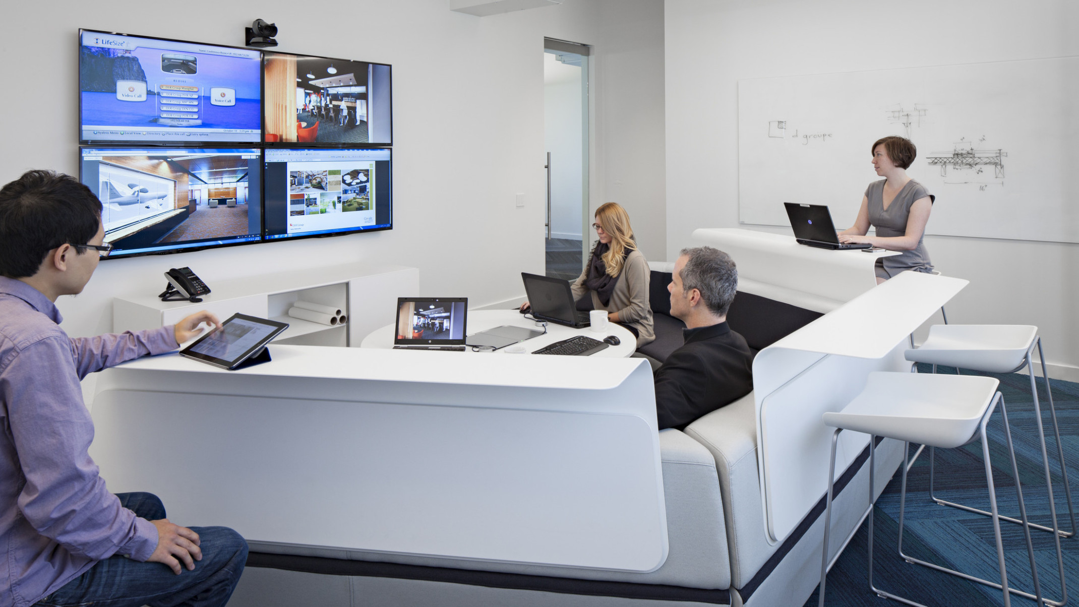 team collaborating with multiple screens, technology, and tiered seating in white conference room