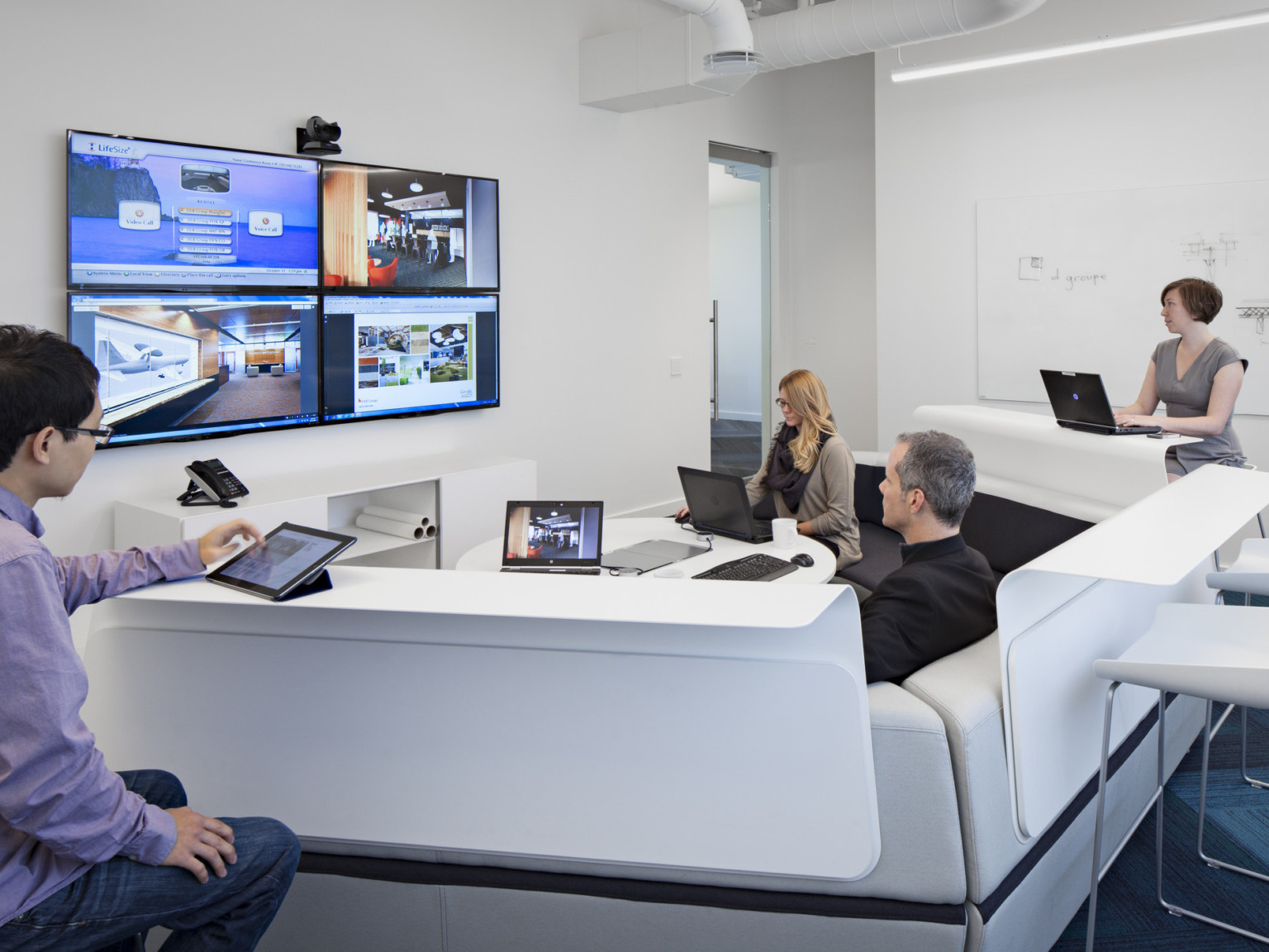 team collaborating with multiple screens, technology, and tiered seating in white conference room