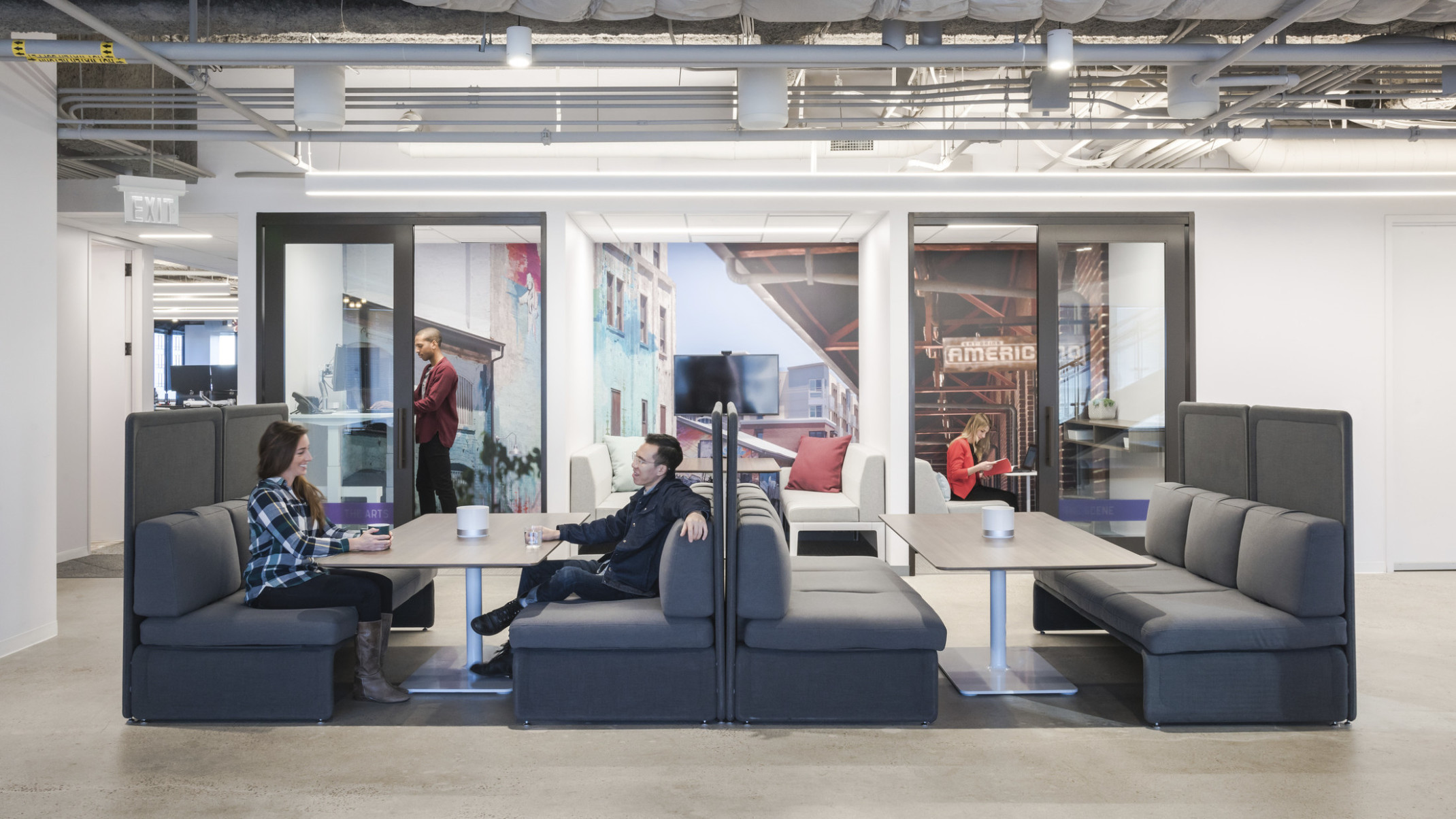people working at booths with private phone booths behind with transparent walls and large graphic murals