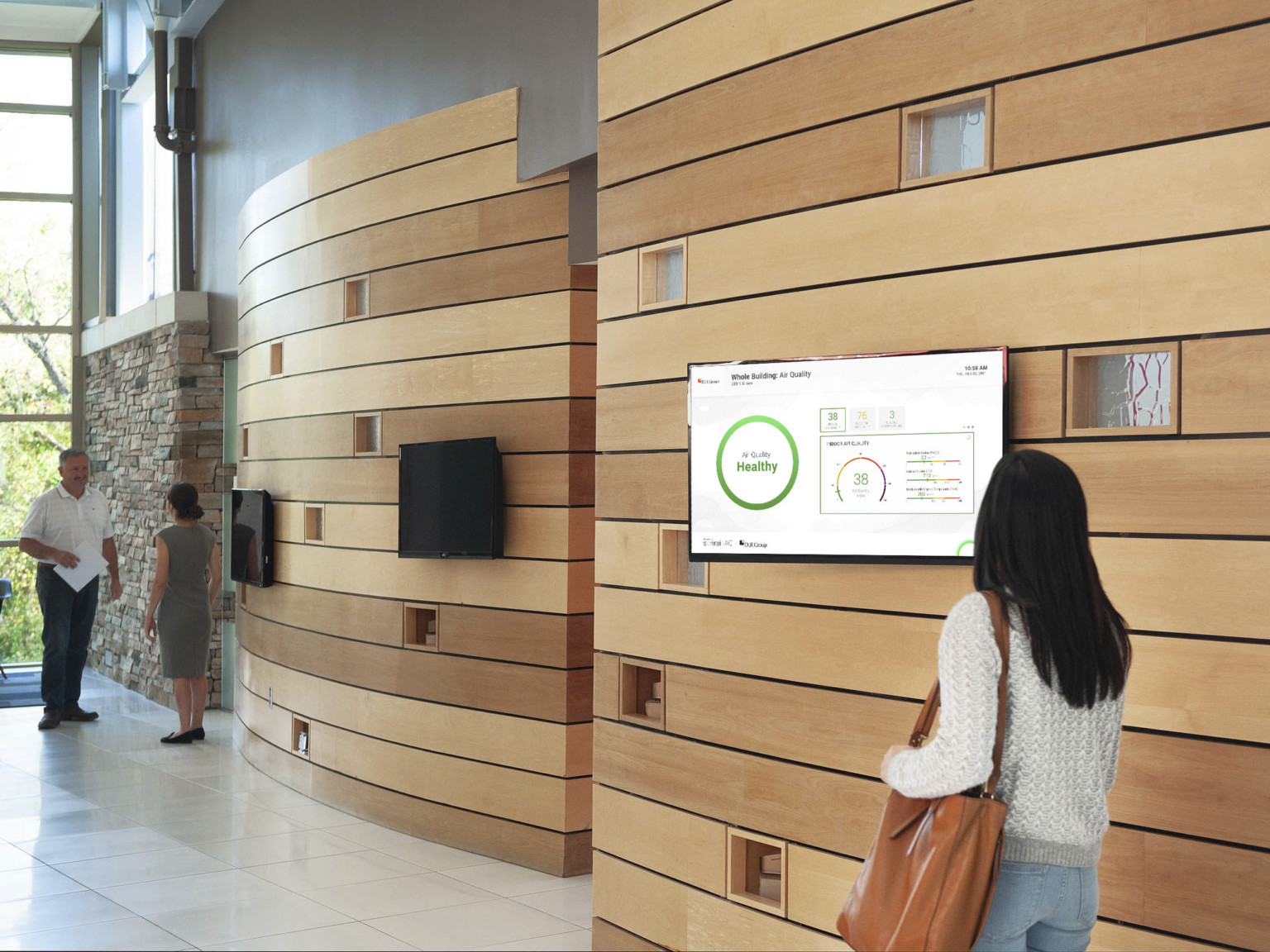 woman walking past interactive screen showing air quality in the workplace with wood panel wall and large window opposite