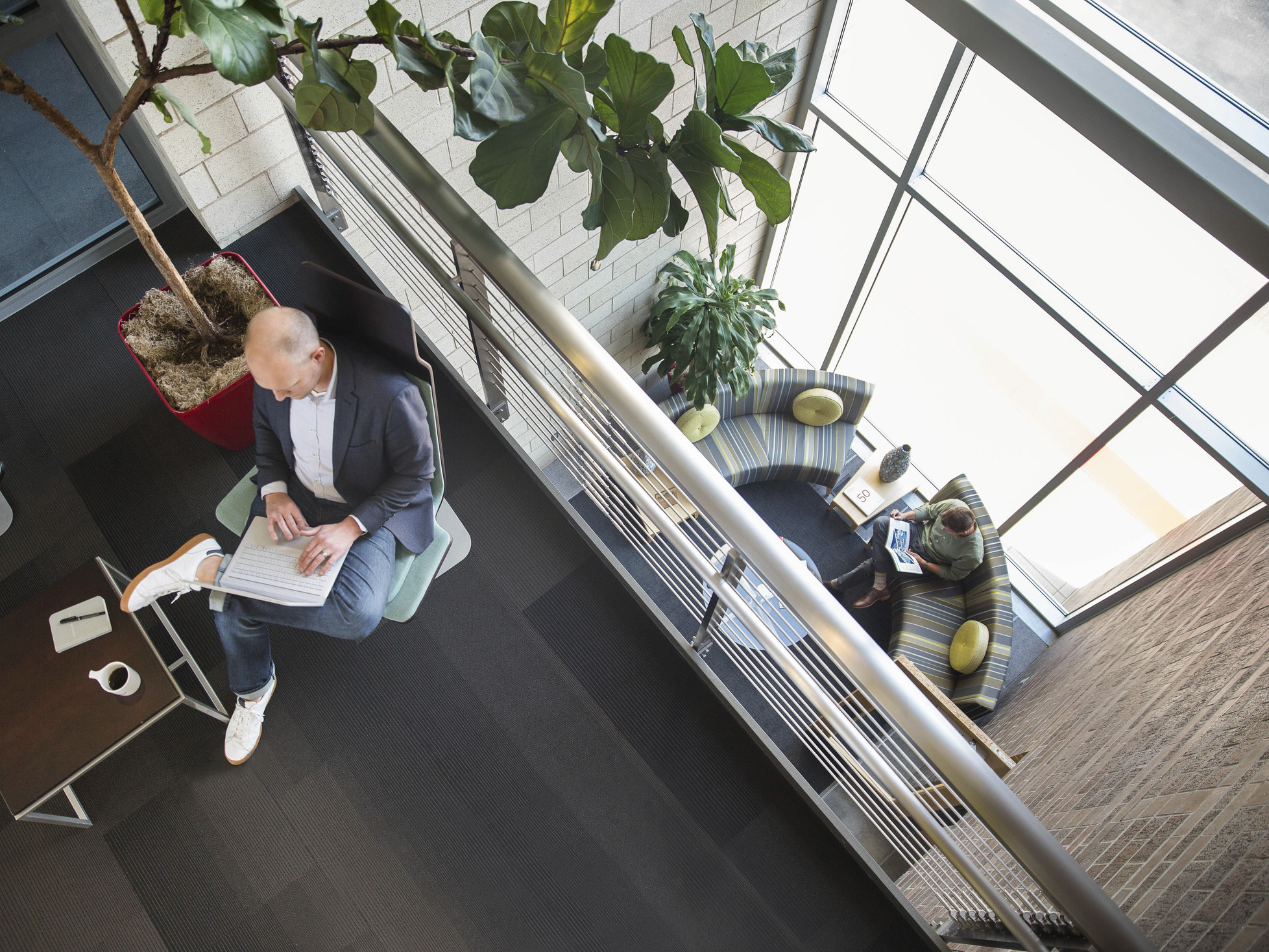 interior balcony looking down to couches by double height windows. Potted plants on both levels