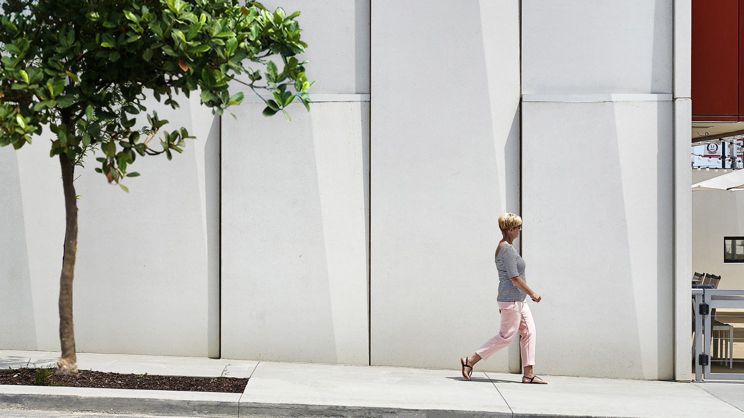 Textured white panels on exterior wall along treelined side walk