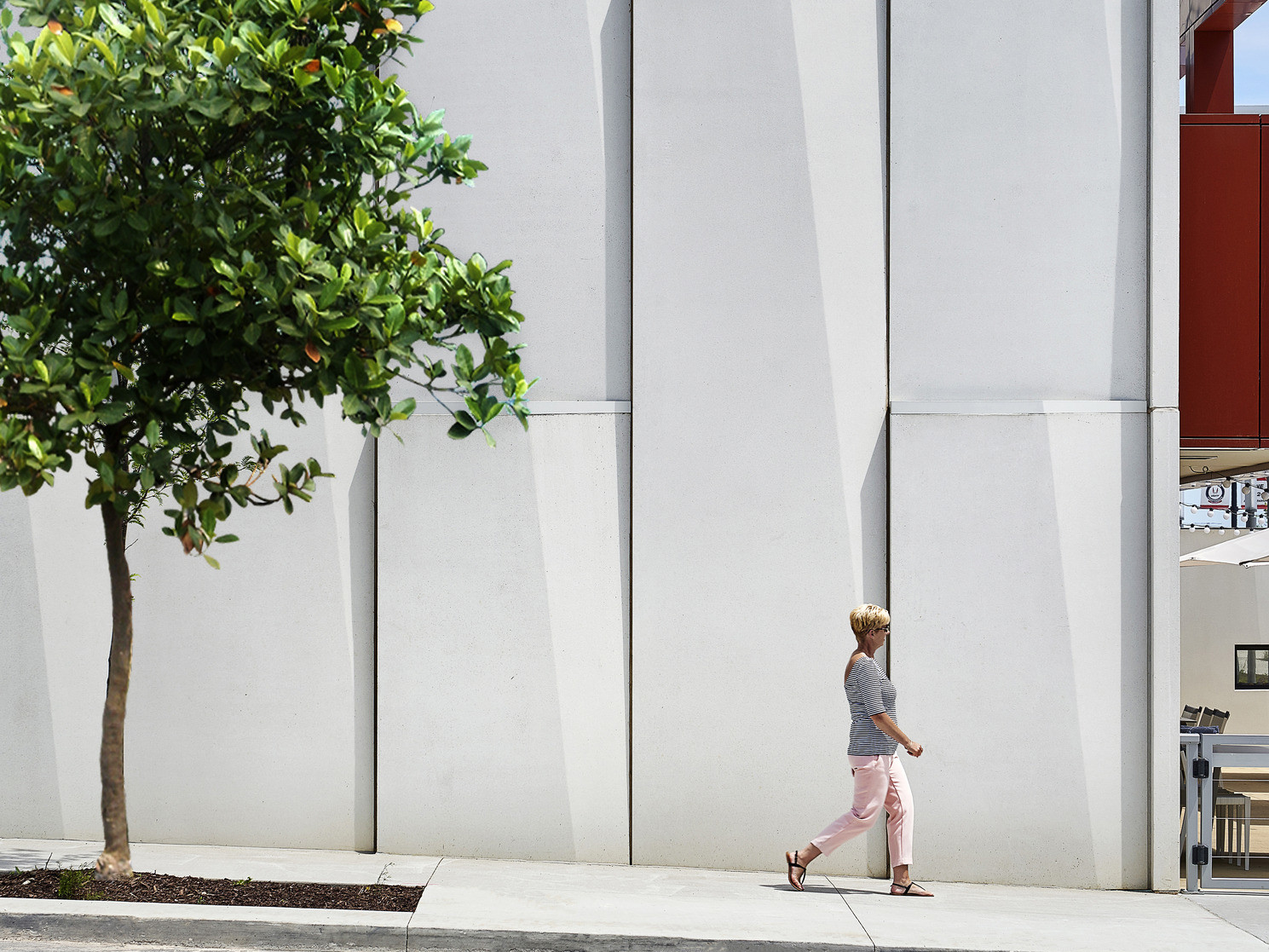 Textured white panels on exterior wall along treelined side walk