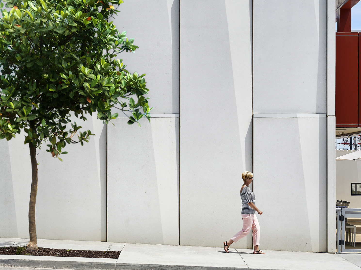 Textured white panels on exterior wall along treelined side walk