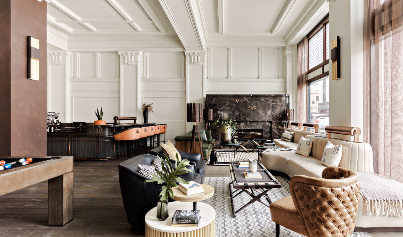 Seating area with arm chairs and cushioned bench along windows. Dark marbled fireplace on white wall with pillars and molding