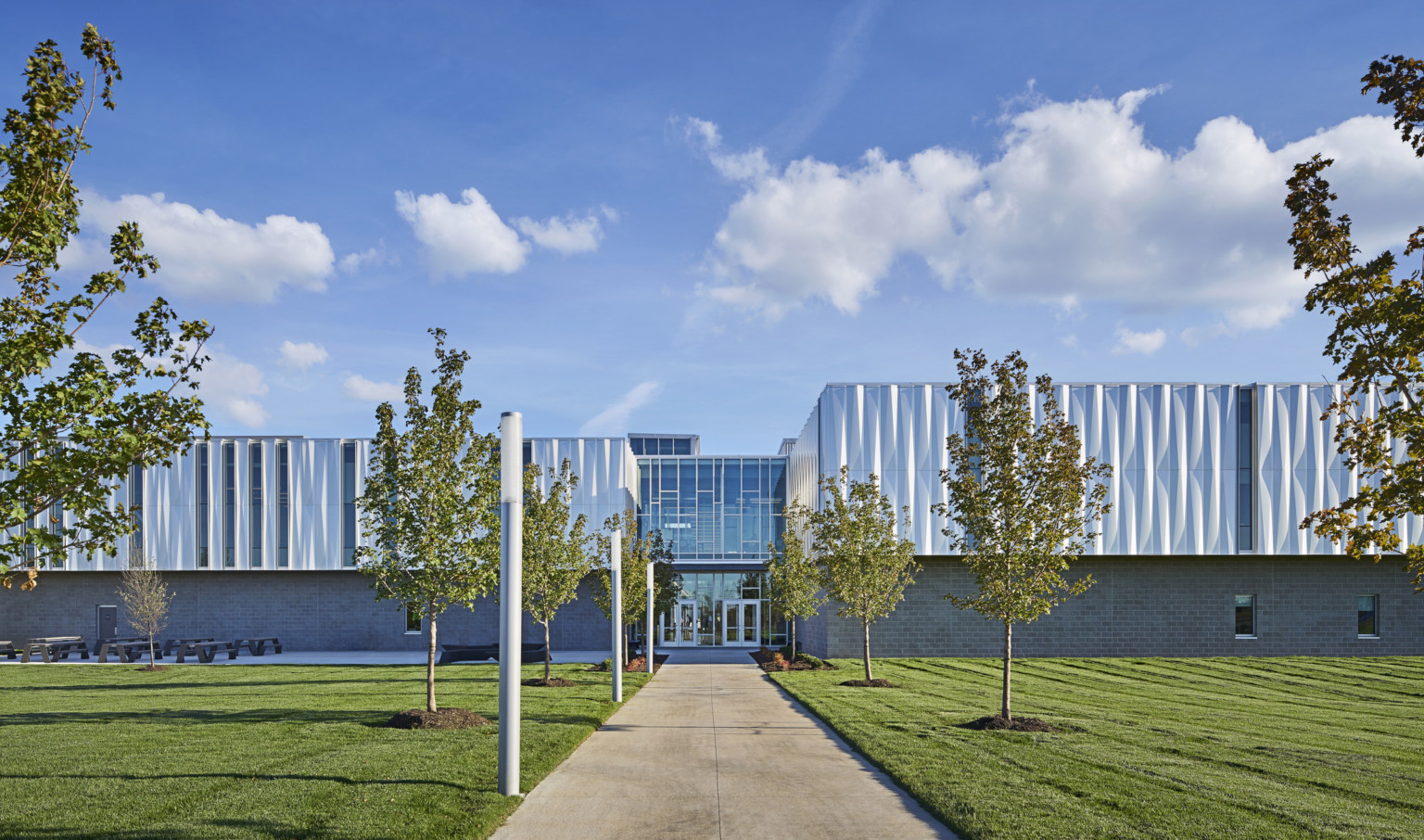 Front view of building looking down a treelined path to the front entrance with 2 sets of glass double doors