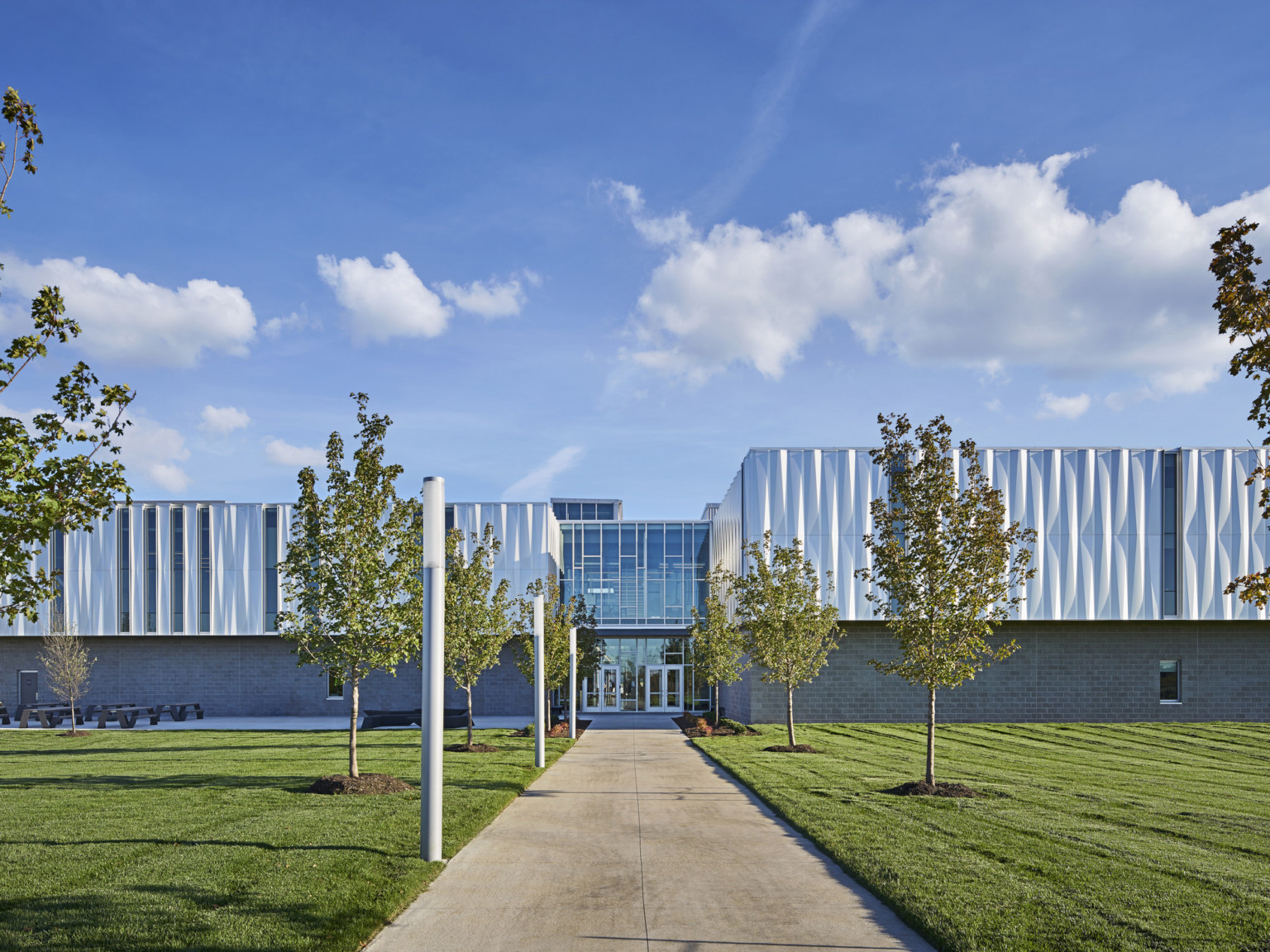 Front view of building looking down a treelined path to the front entrance with 2 sets of glass double doors