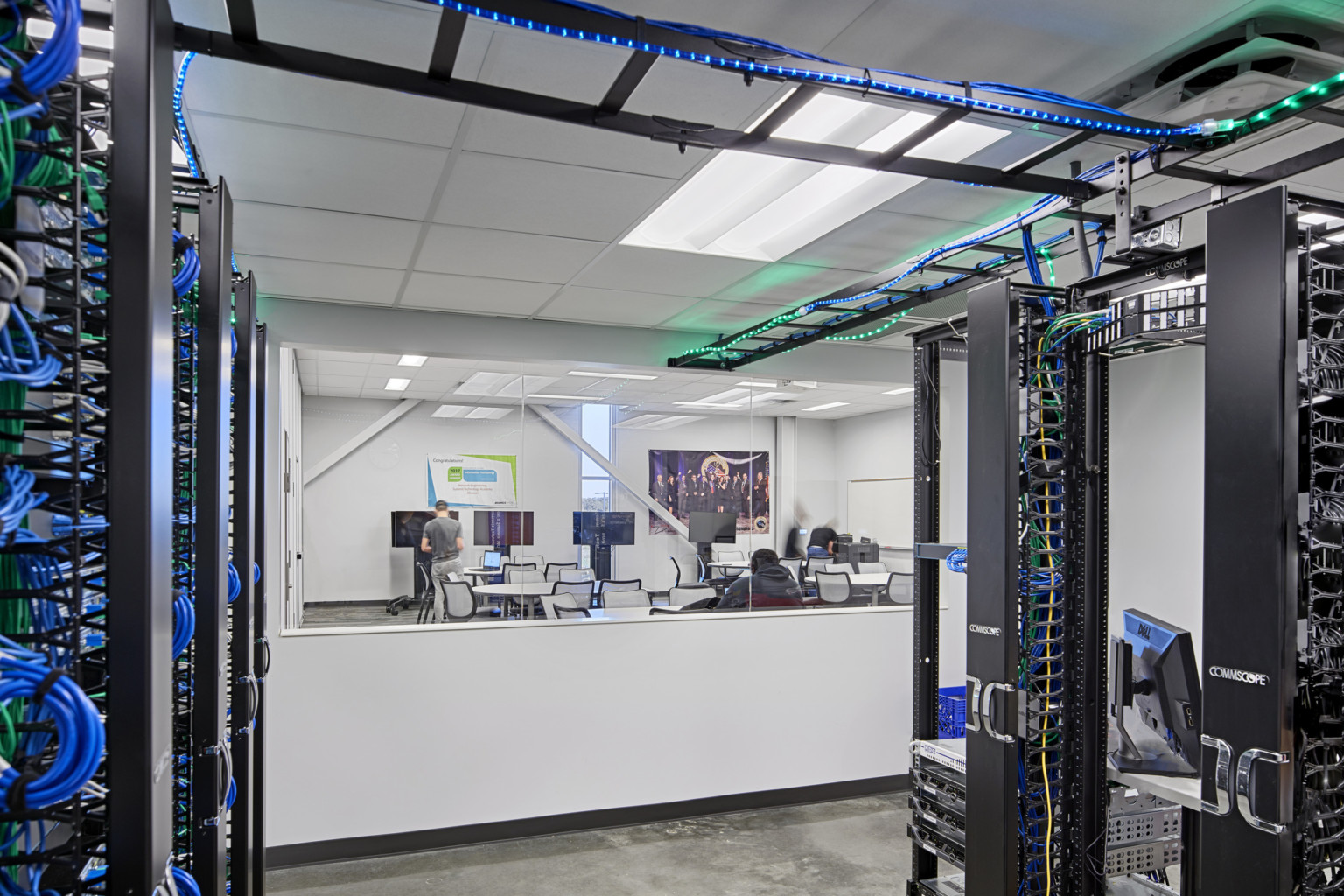 technology room with server cables at a high school with a window looking into a classroom with round tables and screens