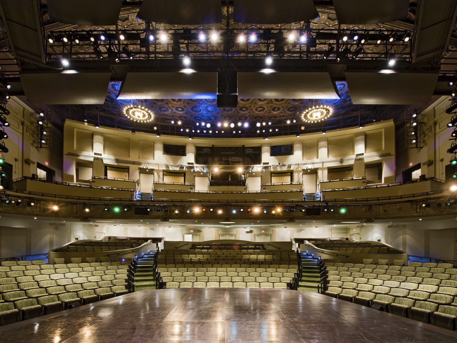The Hanna Theater viewed from stage looking towards yellow patterned theater seats and balcony. Lighting systems frames stage