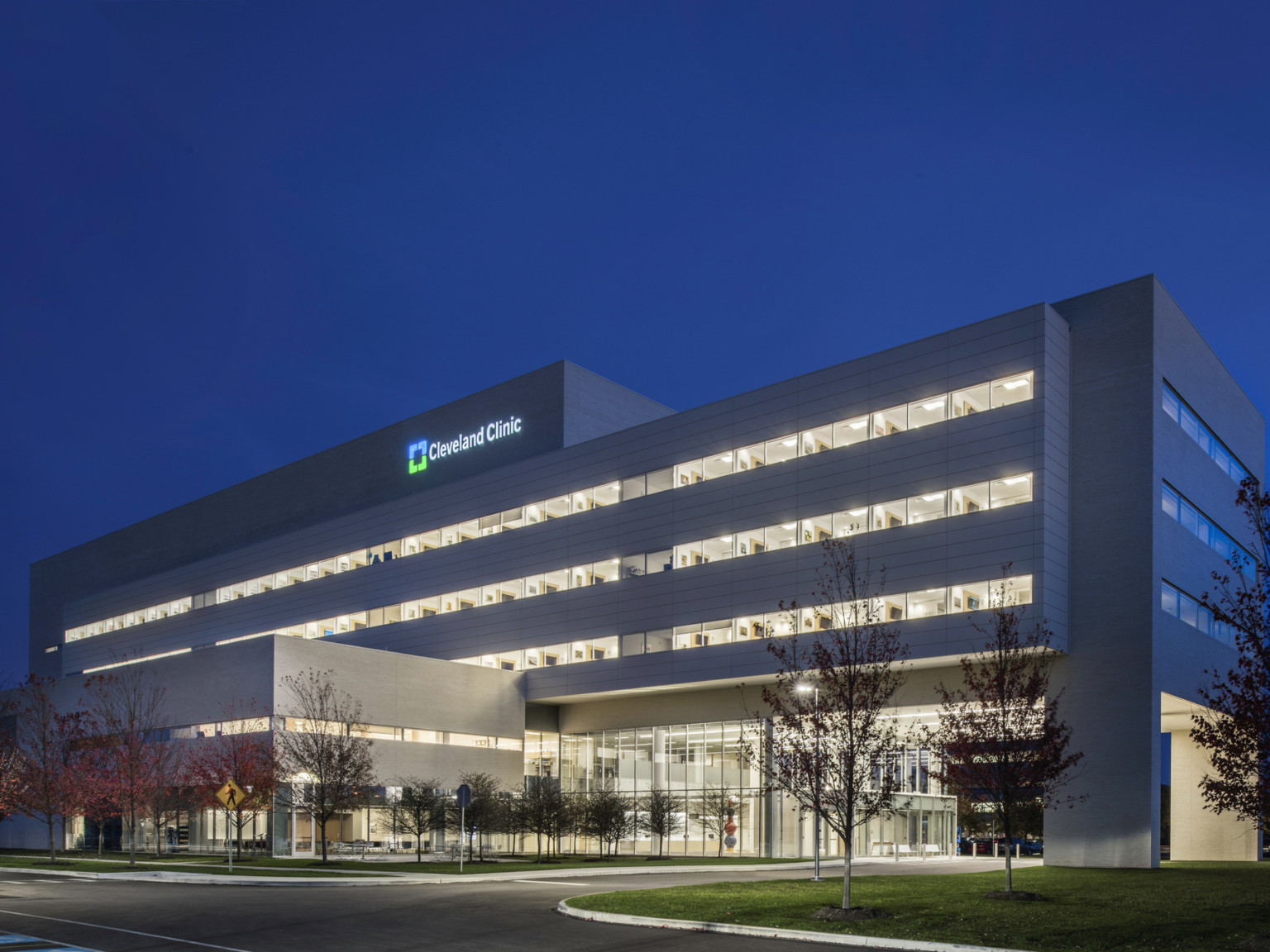 Cleveland Clinic Avon Inpatient Bed Tower illuminated at night seen from across the street facing drive up glass doors