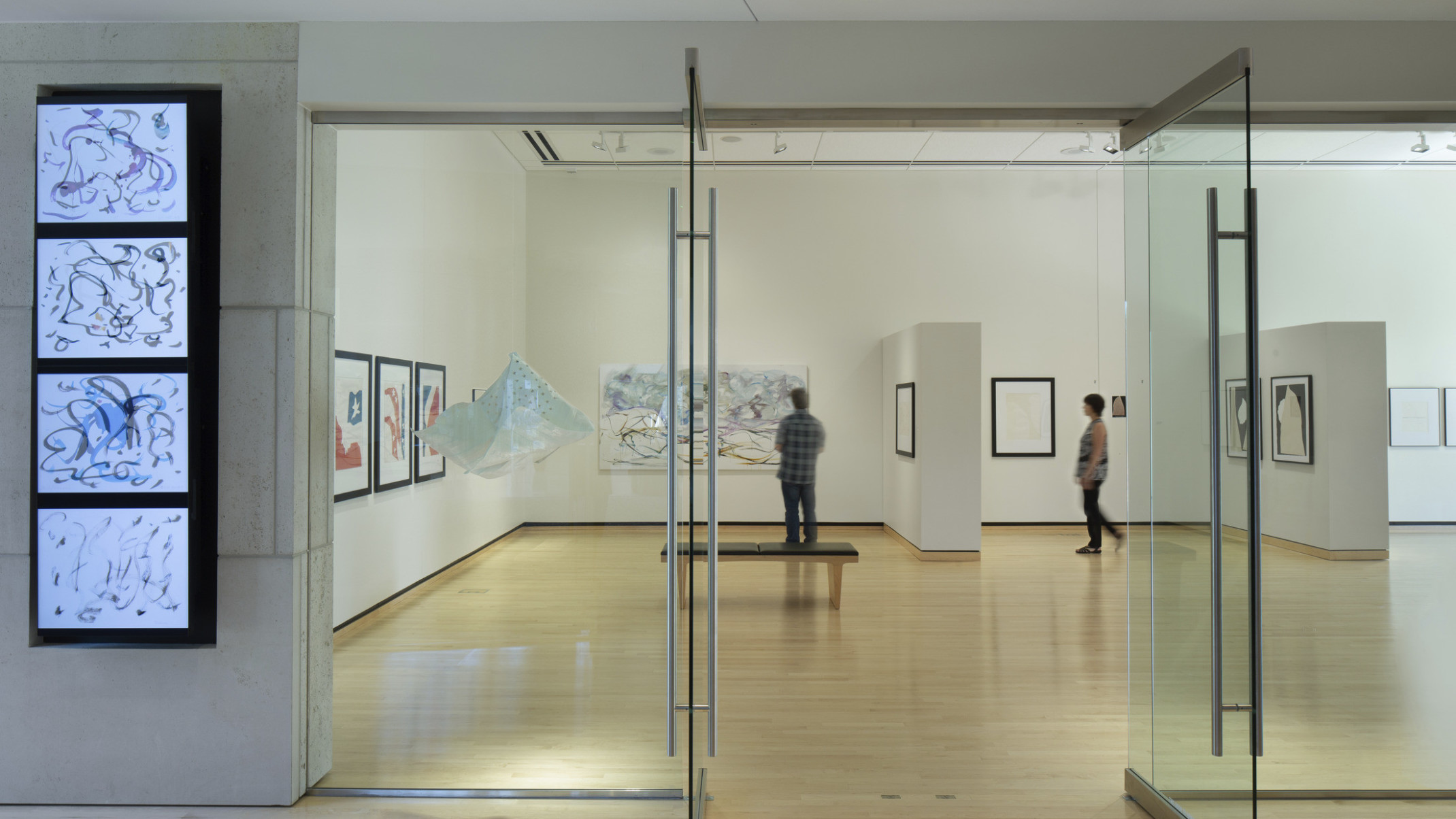 Washburn University Rita Blitt Gallery Addition. Glass doors, interactive screen, left, warm wood floors, and white walls