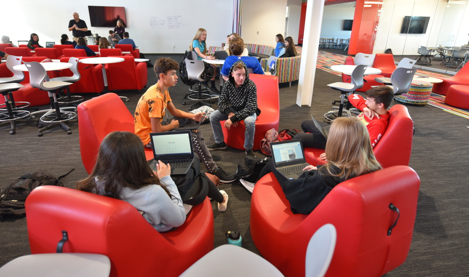 Students working on laptops in red ergonomic chairs in a large open learning space with flexible seating Students working on laptops in red ergonomic chairs in a large open learning space with flexible seating