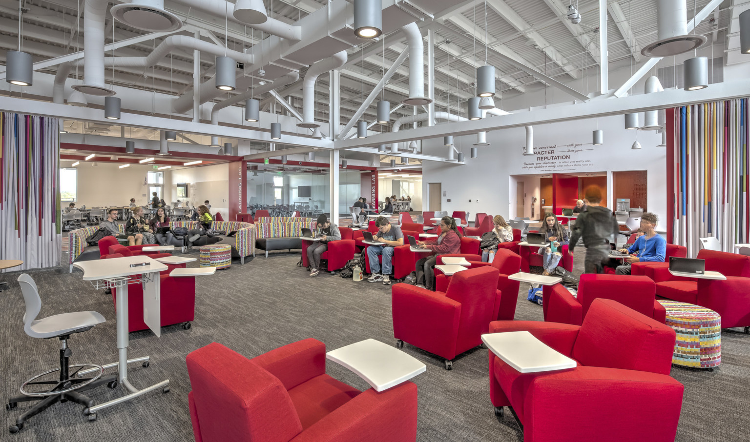 Large carpeted white room with red armchairs. Striped accent walls. Exposed ductwork and hanging pendant lights overhead