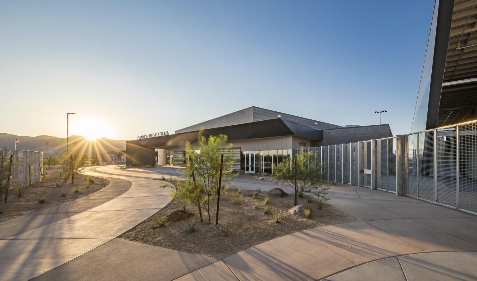 Single story beige building with angular black roof and canopy. Canyon View Arena sign over doors. Fence connects to building Single story beige building with angular black roof and canopy. Canyon View Arena sign over doors. Fence connects to building