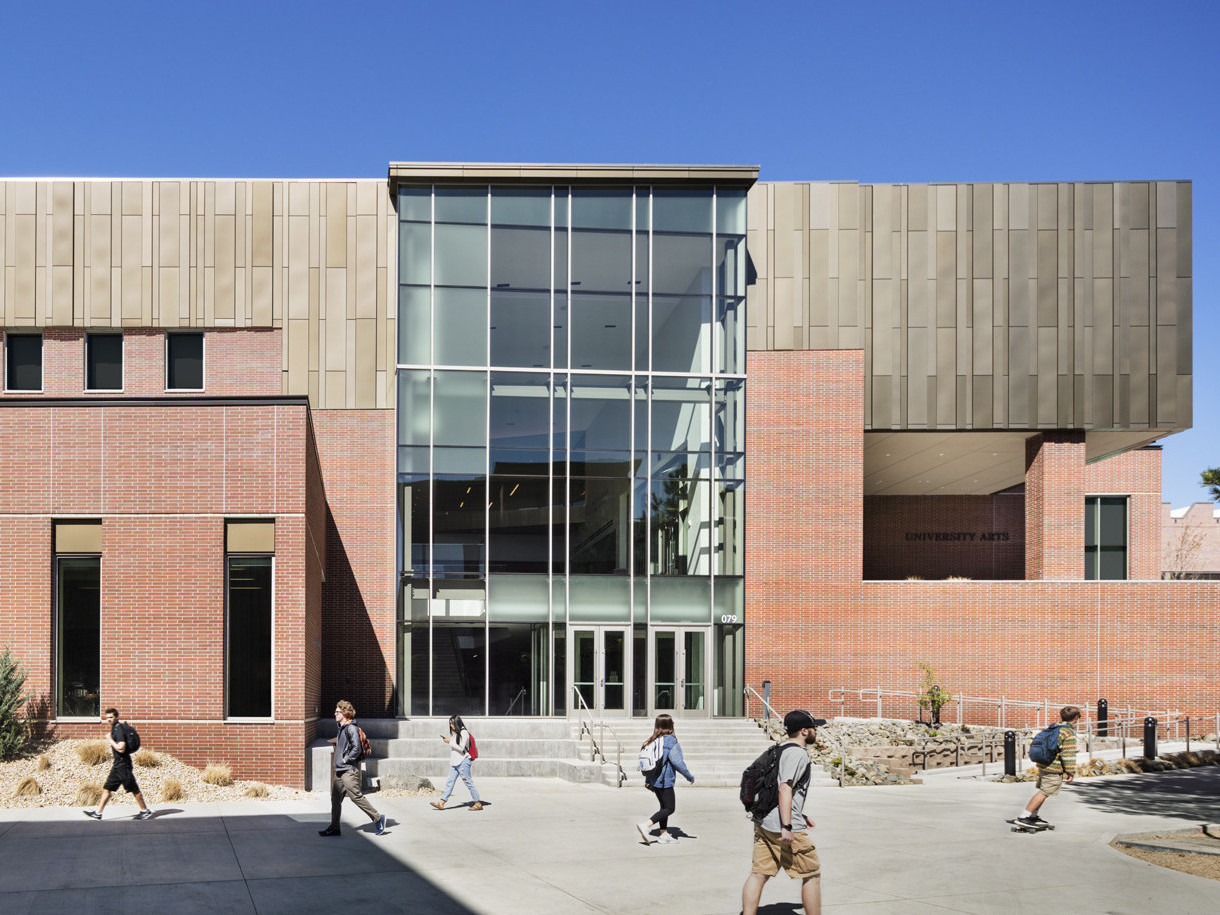 Exterior view of brick building with wood paneled accent at top level. A central glass atrium forms the lobby